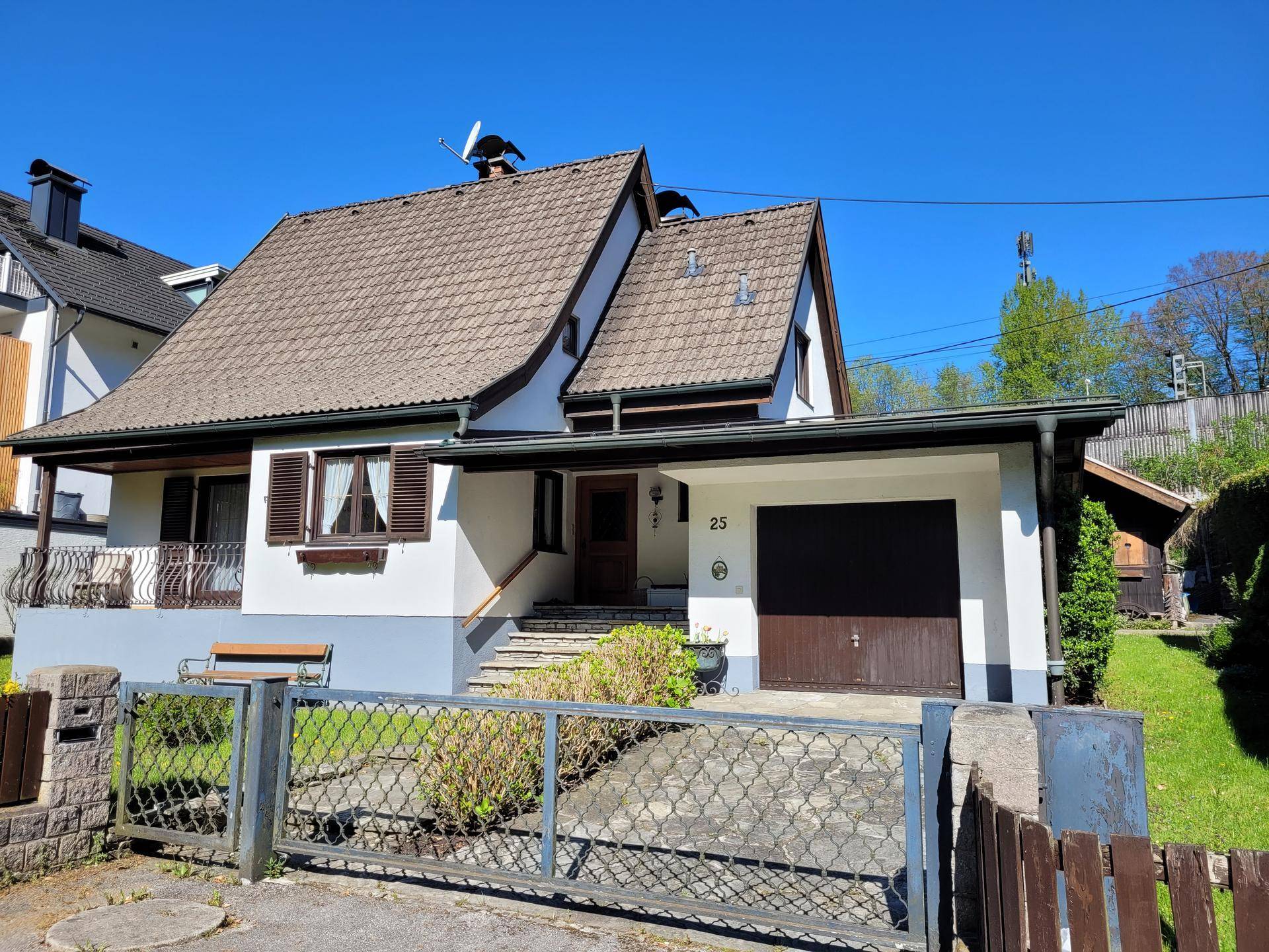 Vorderansicht des Hauses mit Garage, Steintreppe und umzäuntem Vorgarten an einem sonnigen Tag.