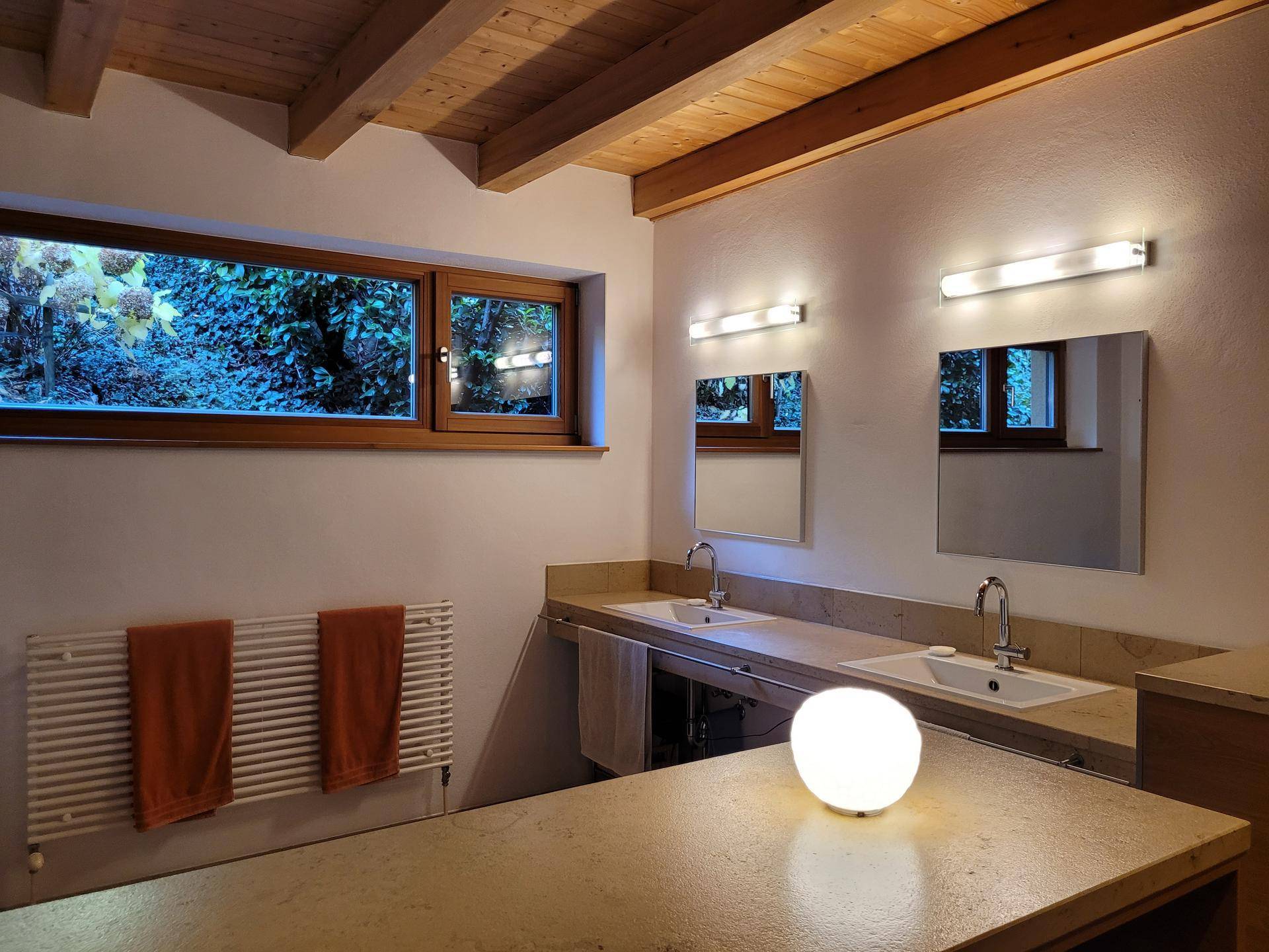 Modernes Badezimmer mit Doppelwaschbecken, beheiztem Handtuchhalter und Fenster mit Blick ins Grüne.