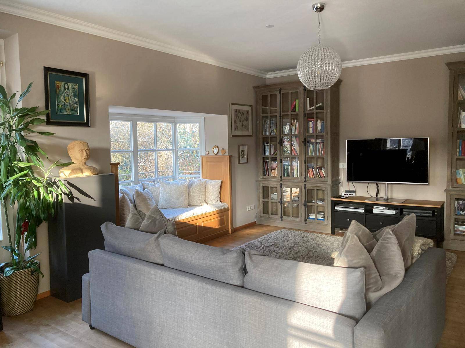 Helles Wohnzimmer mit großem Sofa, Bücherregalen und einem Erkerfenster mit Sitzbank.