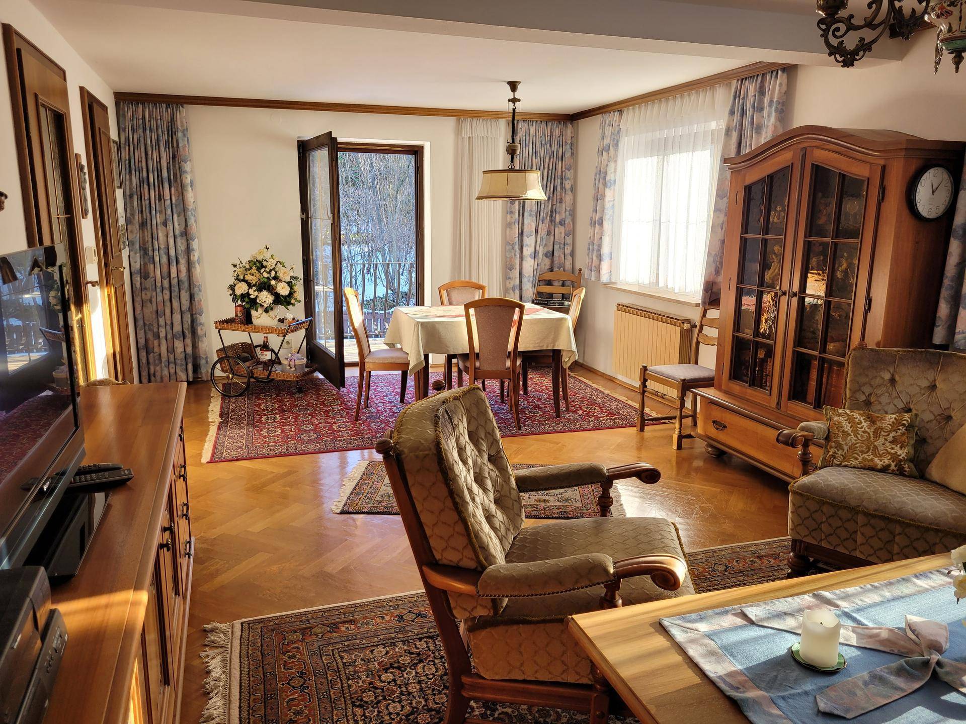 Gemütlicher Wohn-Essbereich mit Parkettboden, traditionellen Möbeln und Zugang zum Balkon.
