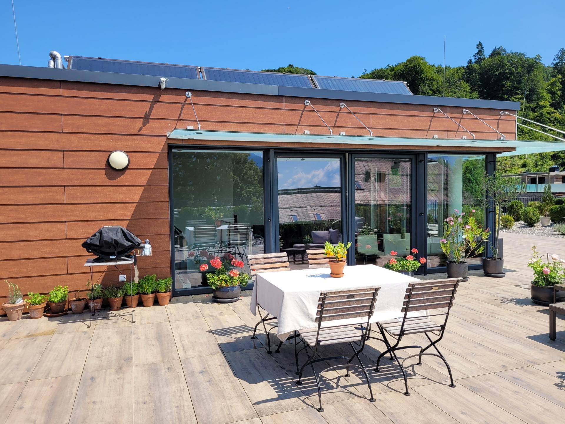 Geräumige Terrasse mit Esstisch, Grill und Zugang zu großen Glasfronten des Gebäudes.