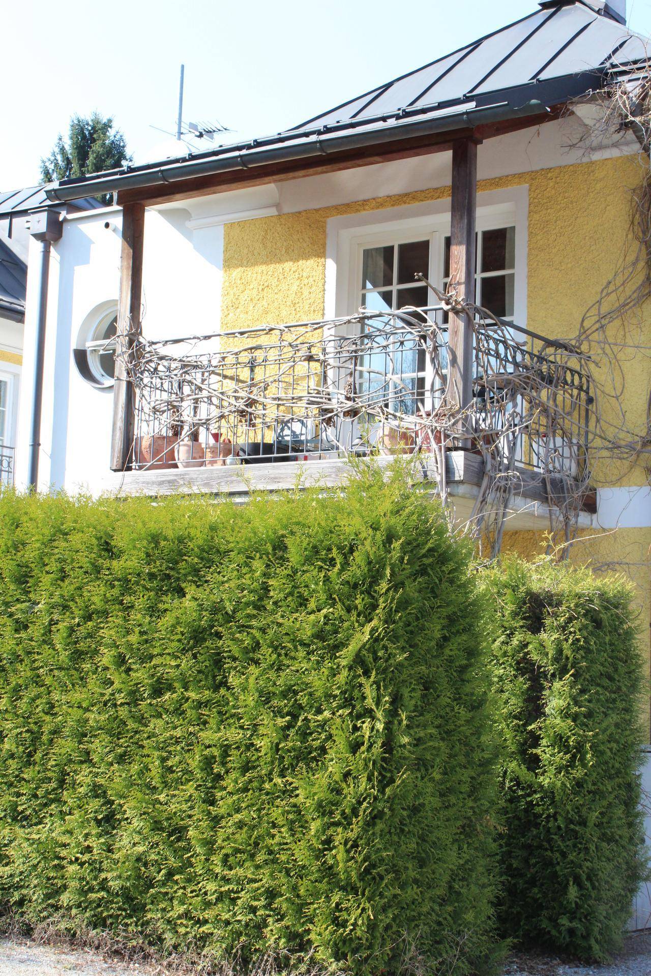 Kleiner Balkon mit schmiedeeisernem Geländer und Blick auf die Hecke.