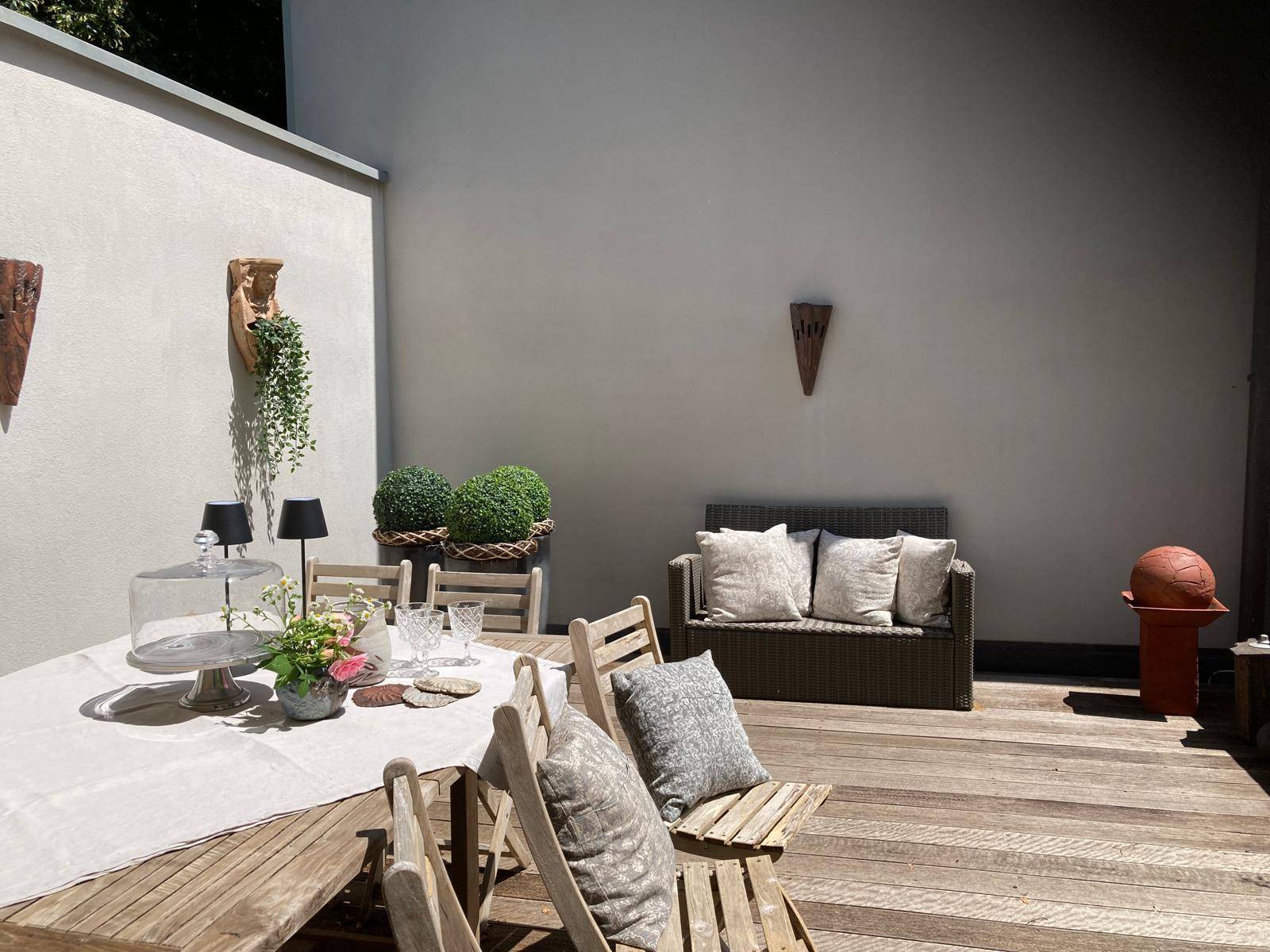 Sonniger Außenbereich mit Holzboden, Esstisch und Lounge-Möbeln.