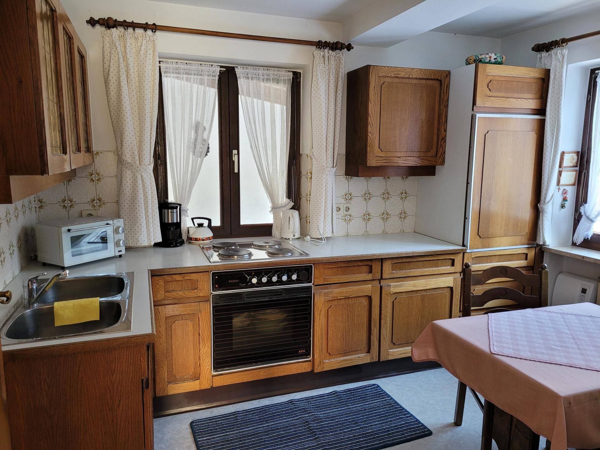 Traditionelle Küche mit Holzschränken, weißer Arbeitsplatte und Blick durch das Fenster.