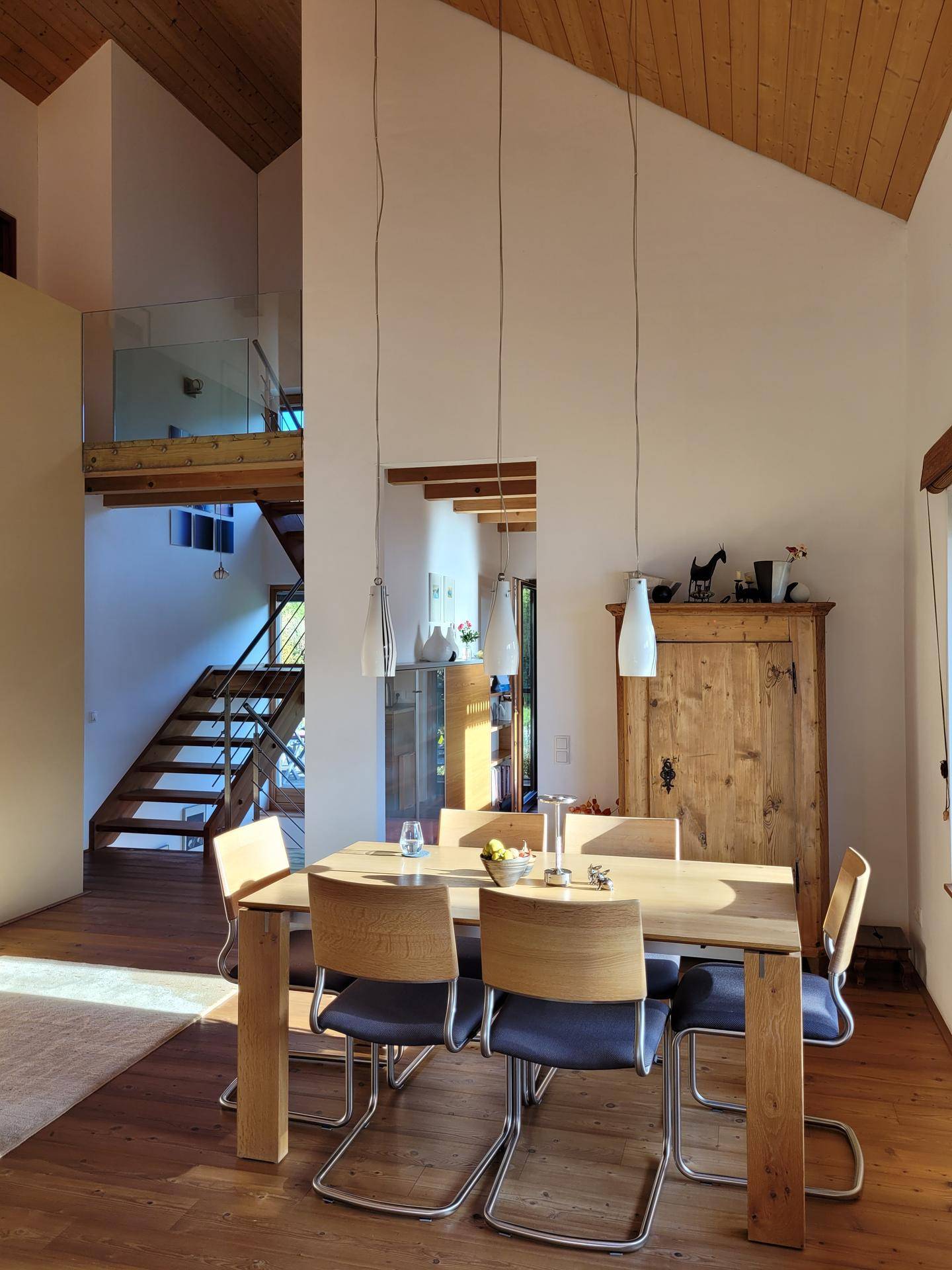 Heller Essbereich mit Holztisch und Stühlen, hohen Decken und Blick auf die offene Treppe zur Galerie.