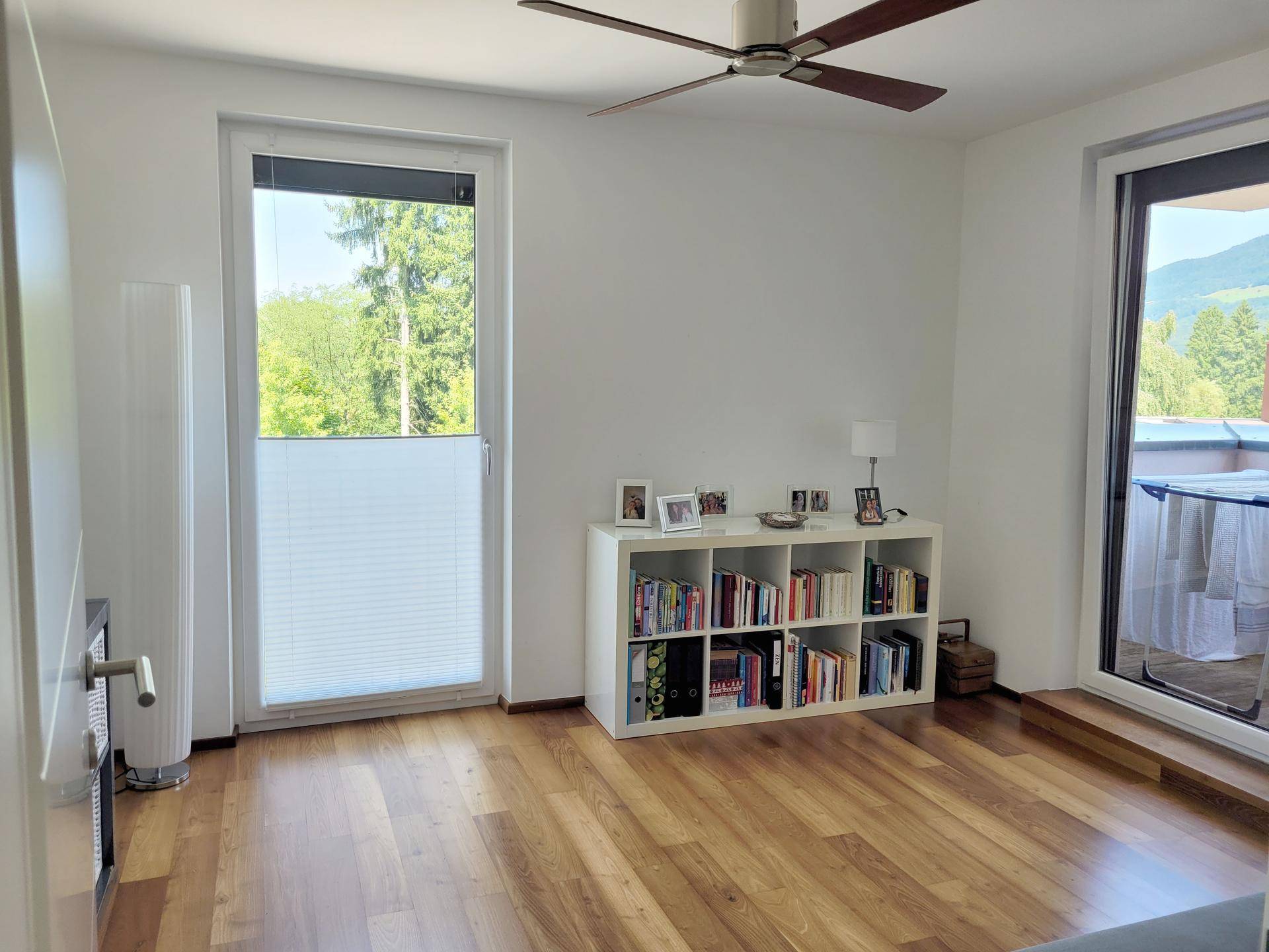 Schlafzimmer mit Holzboden, Deckenventilator und Zugang zu einem Balkon.