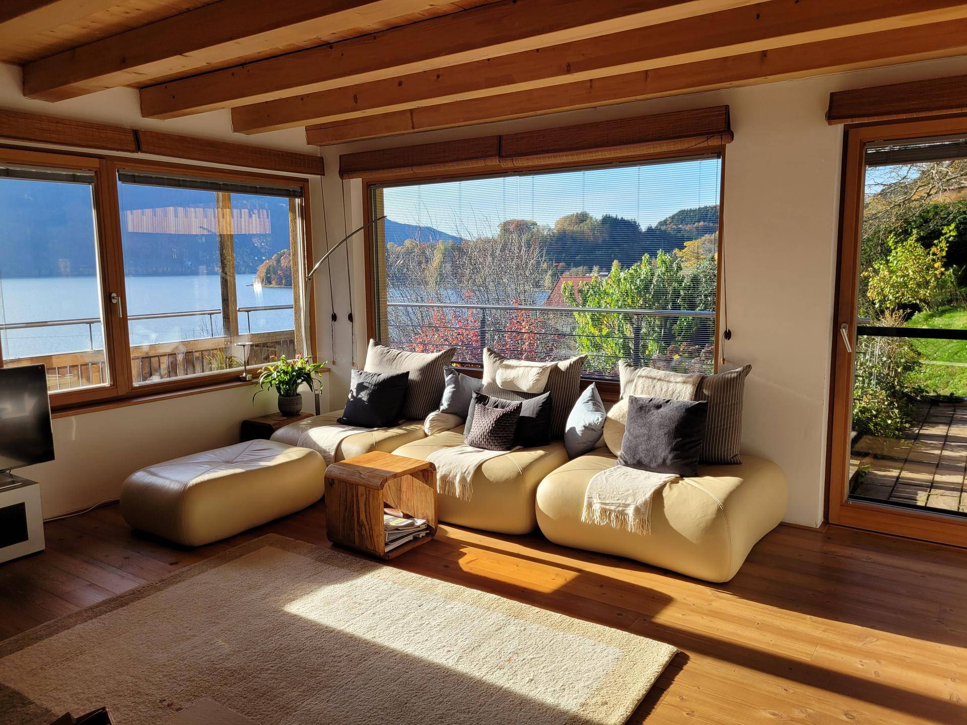 Gemütliches Wohnzimmer mit bequemen Sofas, Holzboden und einem weiten Blick auf den See und die Berge.