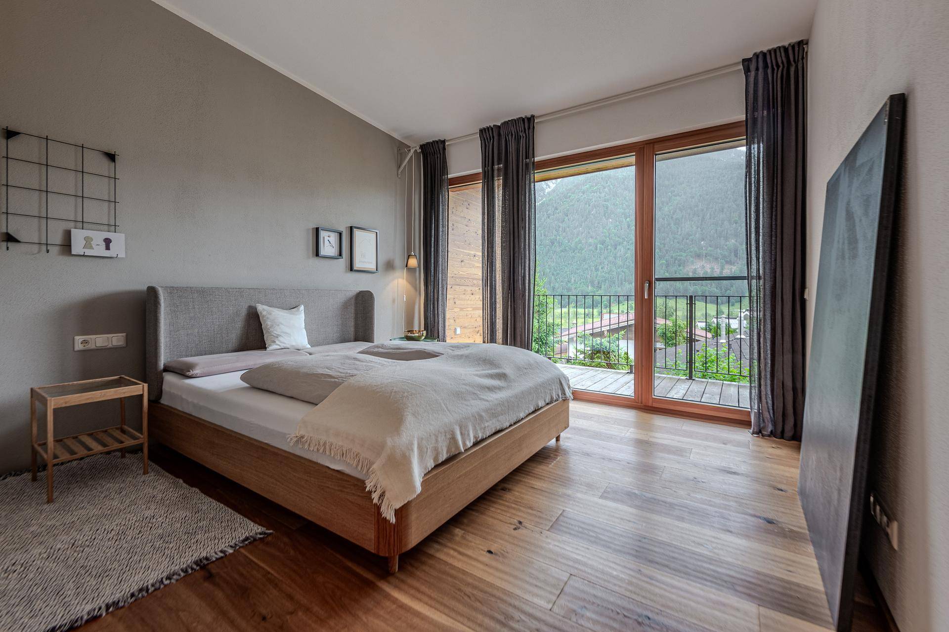 Schlafzimmer mit Doppelbett, Holzboden und bodentiefen Fenstern mit herrlichem Bergblick.