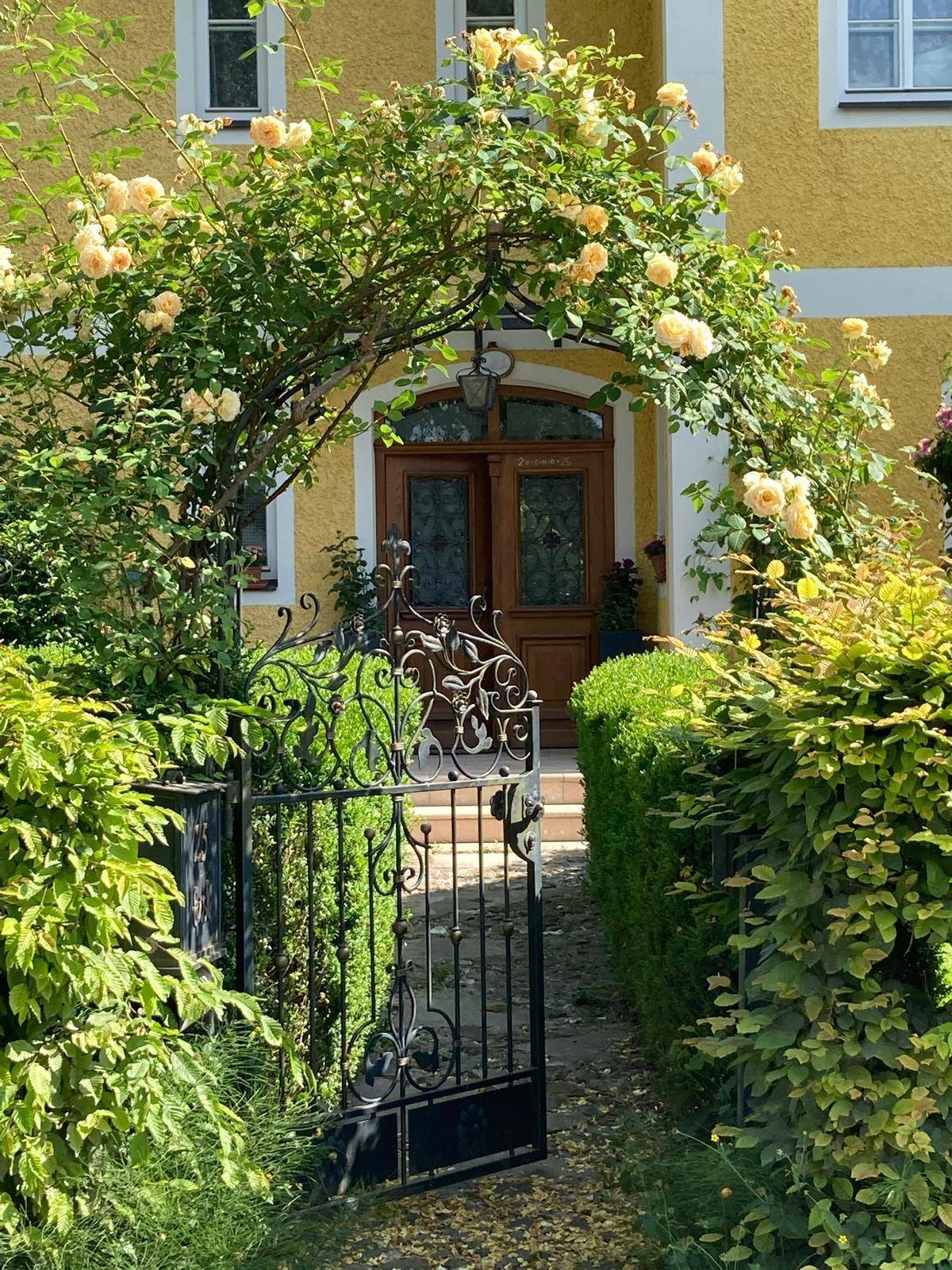 Malerischer Eingangsbereich mit schmiedeeisernem Tor und Rosenbogen zur Haustür.