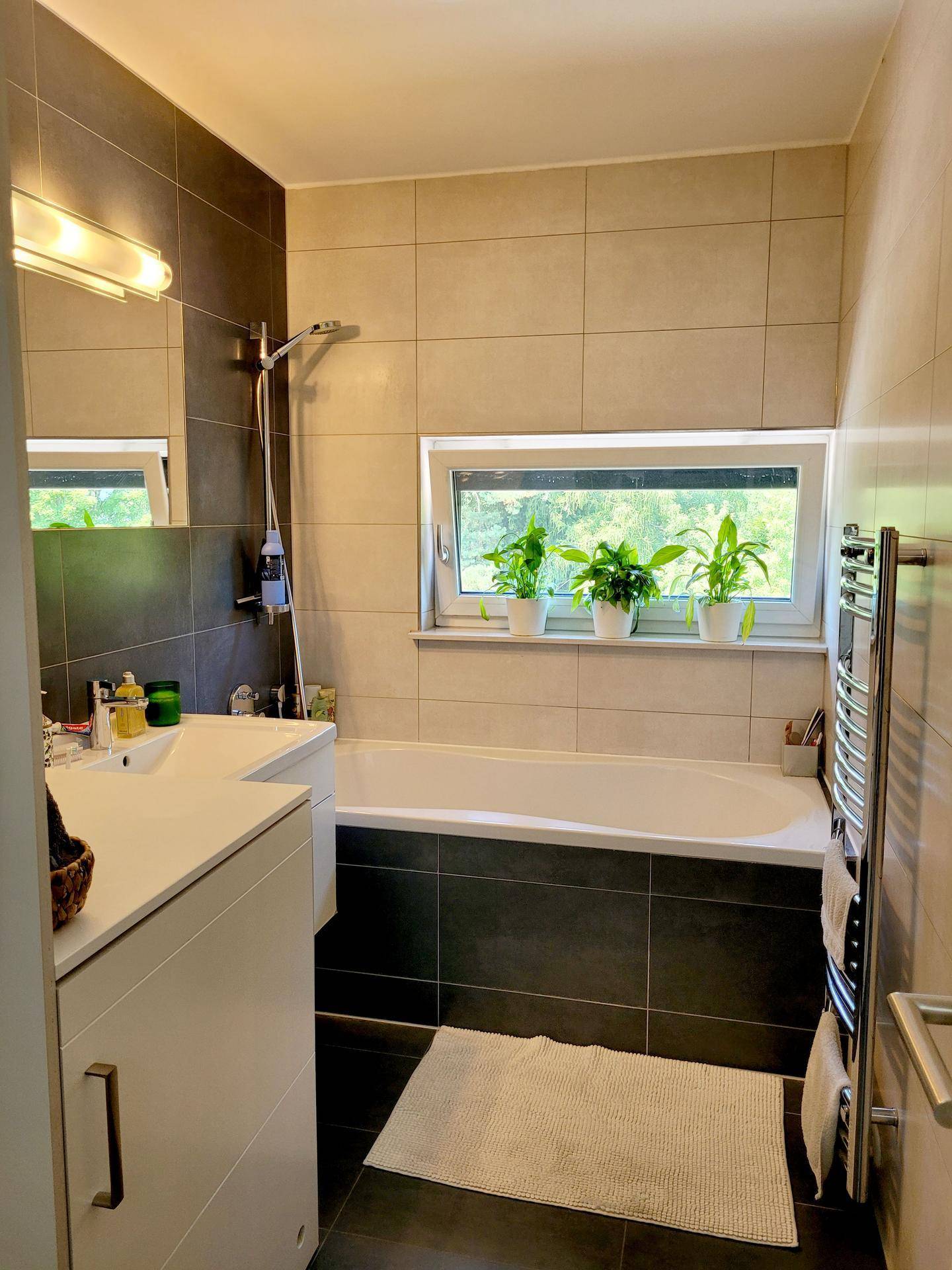 Modernes Badezimmer mit Badewanne, Dusche, beheiztem Handtuchhalter und Fenster.