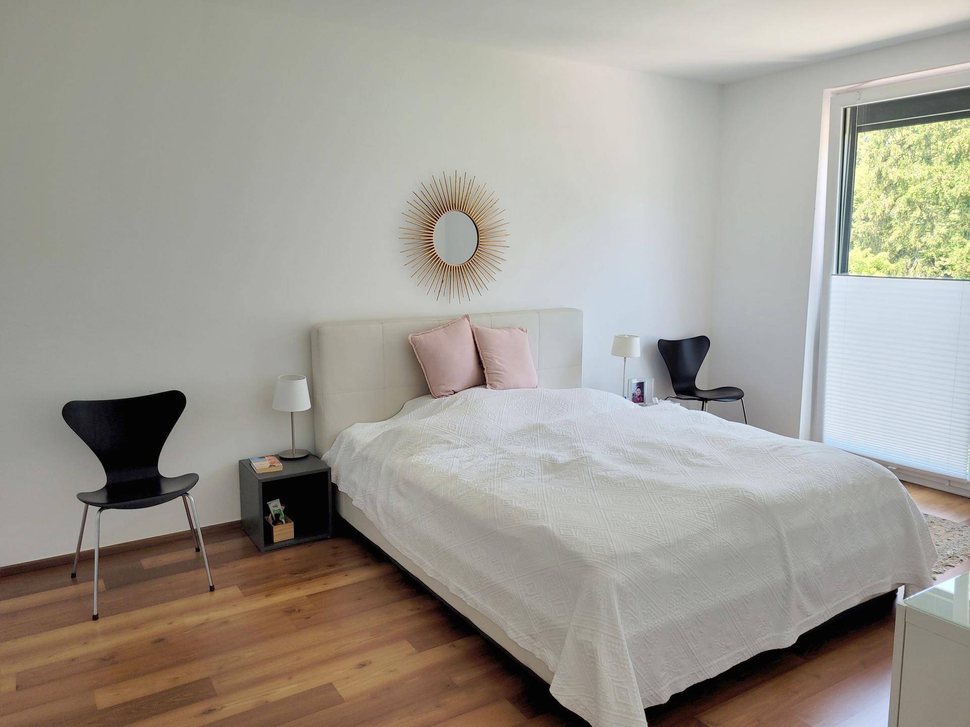 Helles Schlafzimmer mit Doppelbett, Holzboden und Fenster mit Blick ins Grüne.
