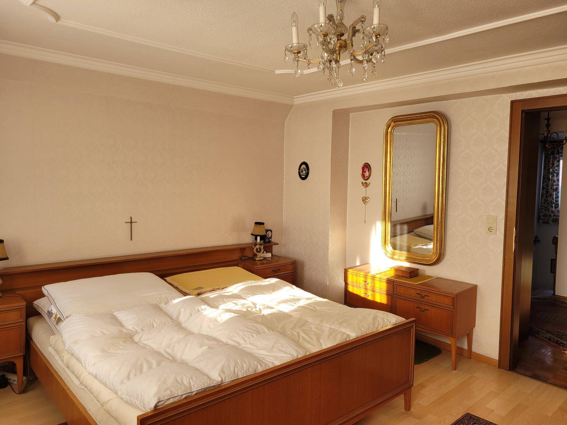 Schlafzimmer mit Doppelbett, Holzmöbeln, Parkettboden und Kronleuchter an der Decke.
