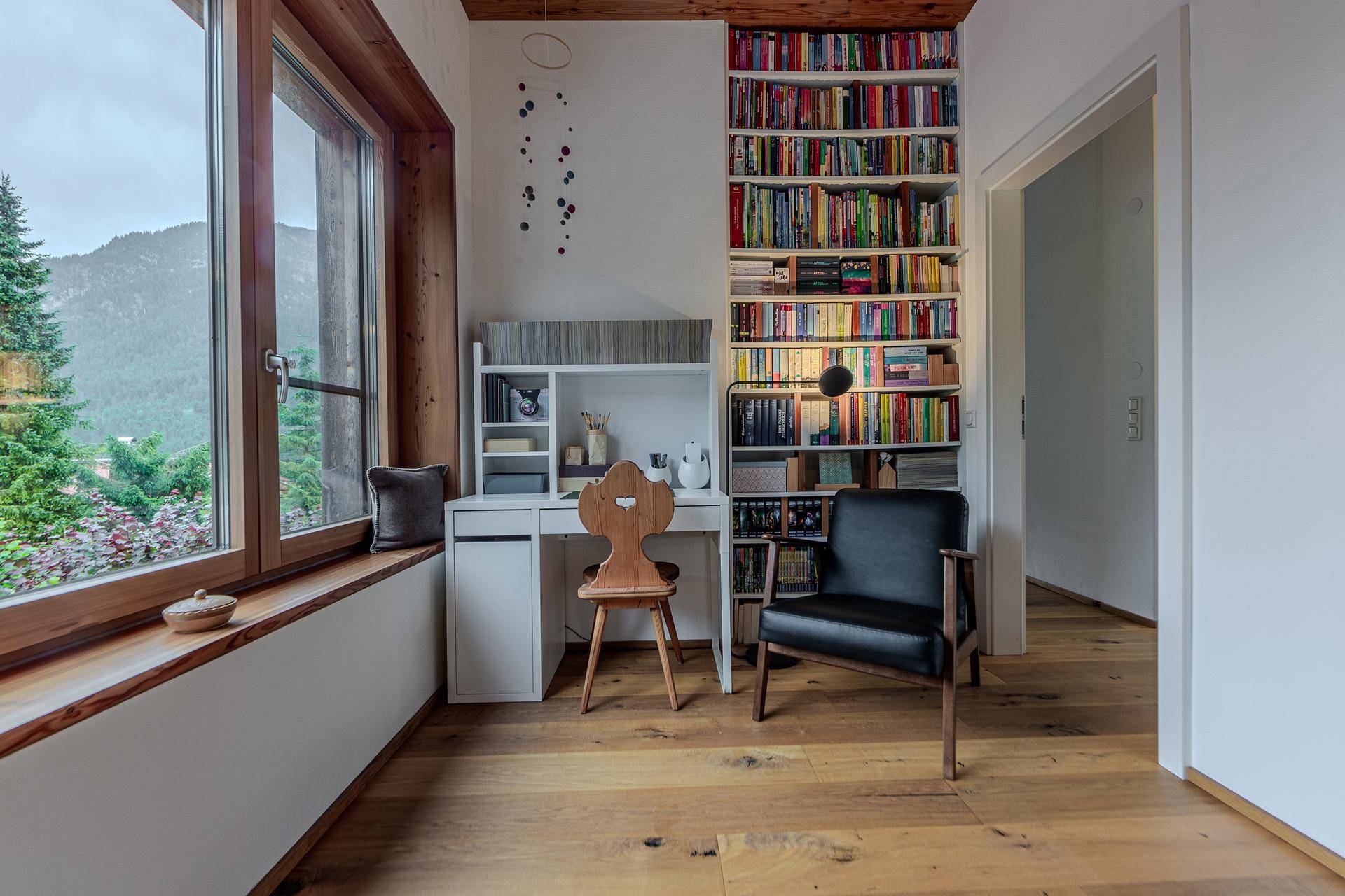 Ruhiges Arbeitszimmer mit großem Fenster, Bücherregal und Holzboden, ideal für konzentriertes Arbeiten.