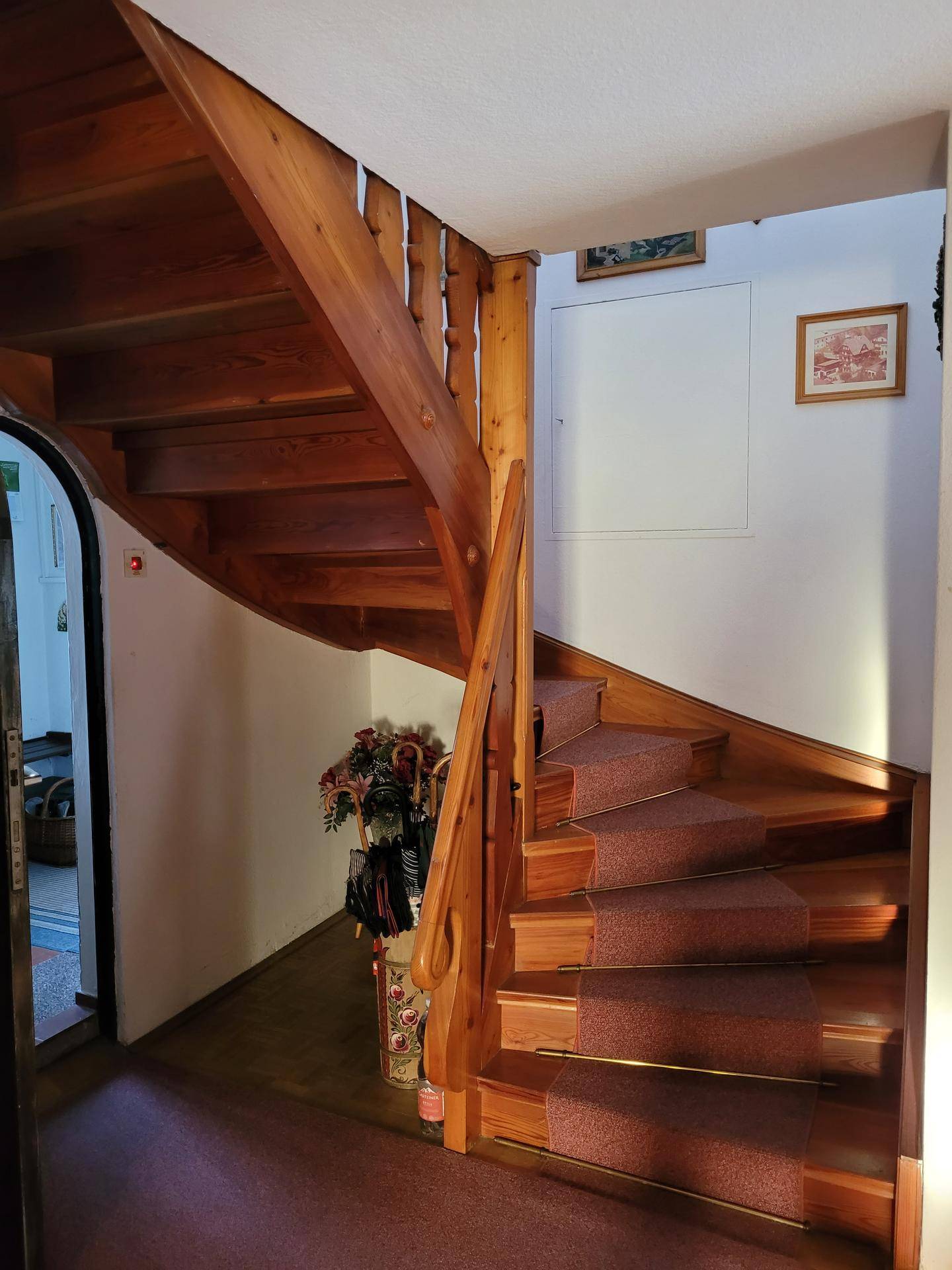 Holztreppe mit Teppichläufer und geschwungenem Geländer, die in die obere Etage führt.