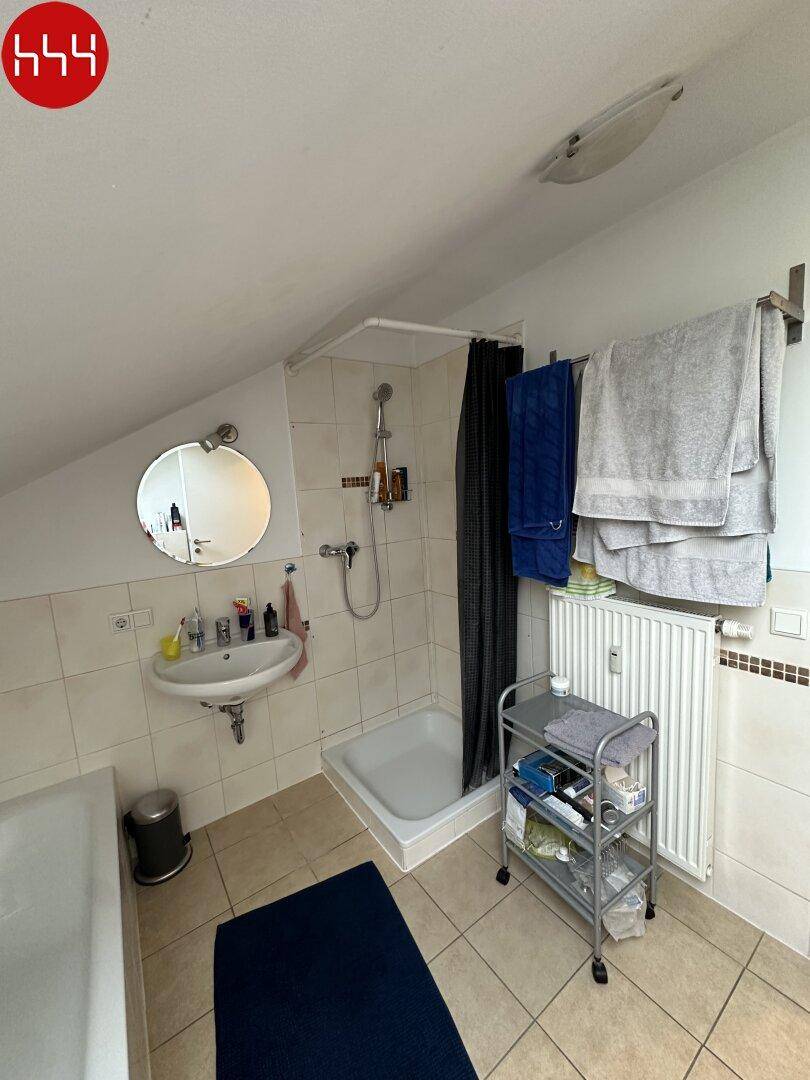 Badezimmer mit Dusche, Waschbecken und Fliesenboden unter der Dachschräge.