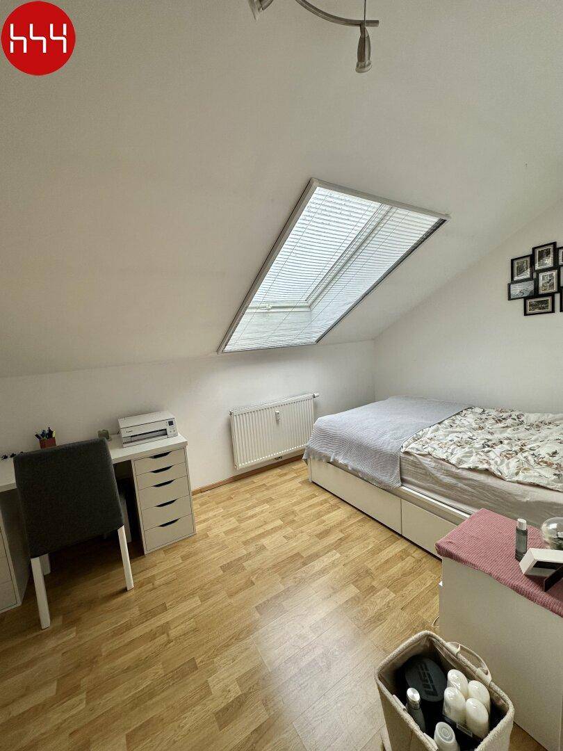 Helles Schlafzimmer mit Schreibtisch, Heizkörper und Dachfenster.