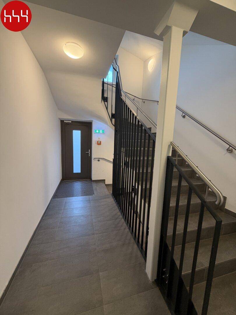 Heller Treppenaufgang im Mehrfamilienhaus mit robustem Fliesenboden und Metallgeländer.