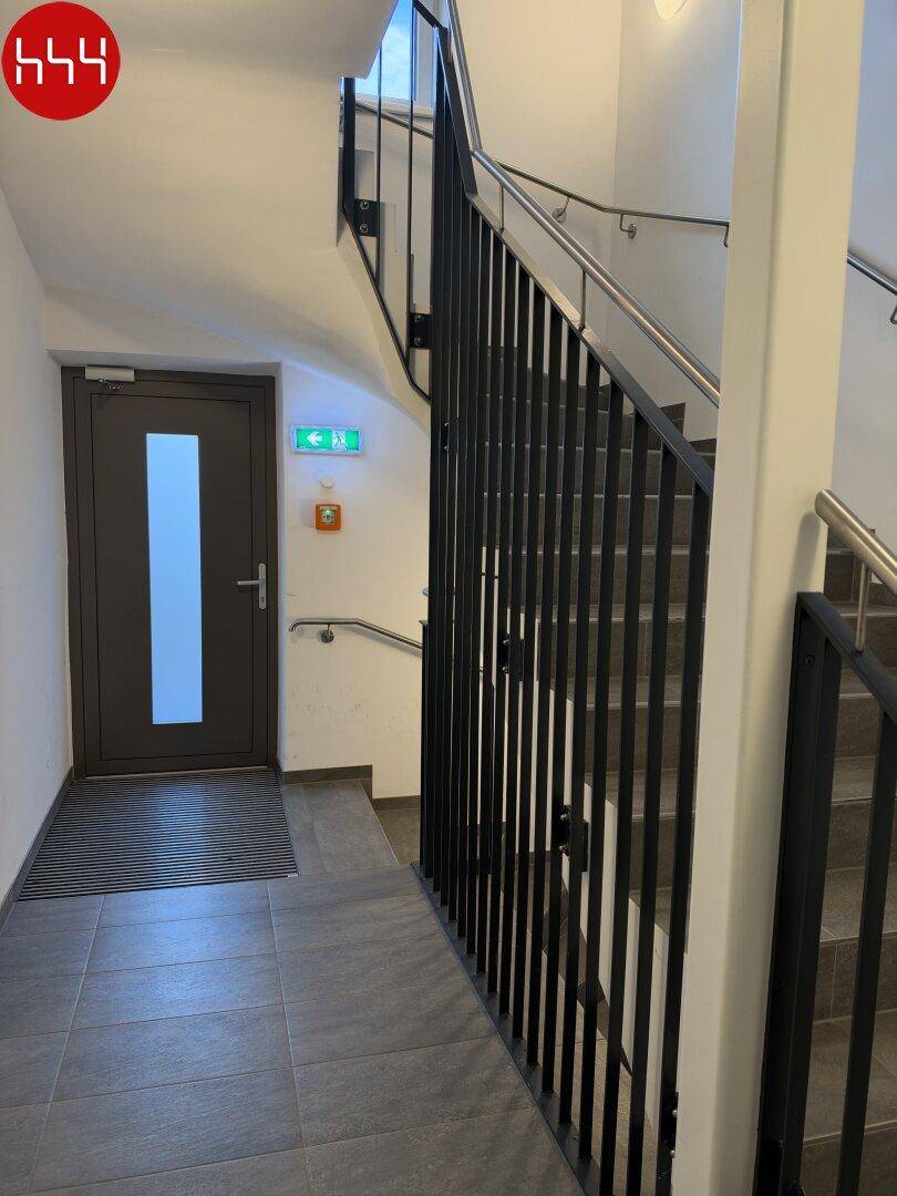 Treppenhaus mit modernem Geländer, Fliesenboden und Zugang zu den Wohneinheiten in einem Neubau.