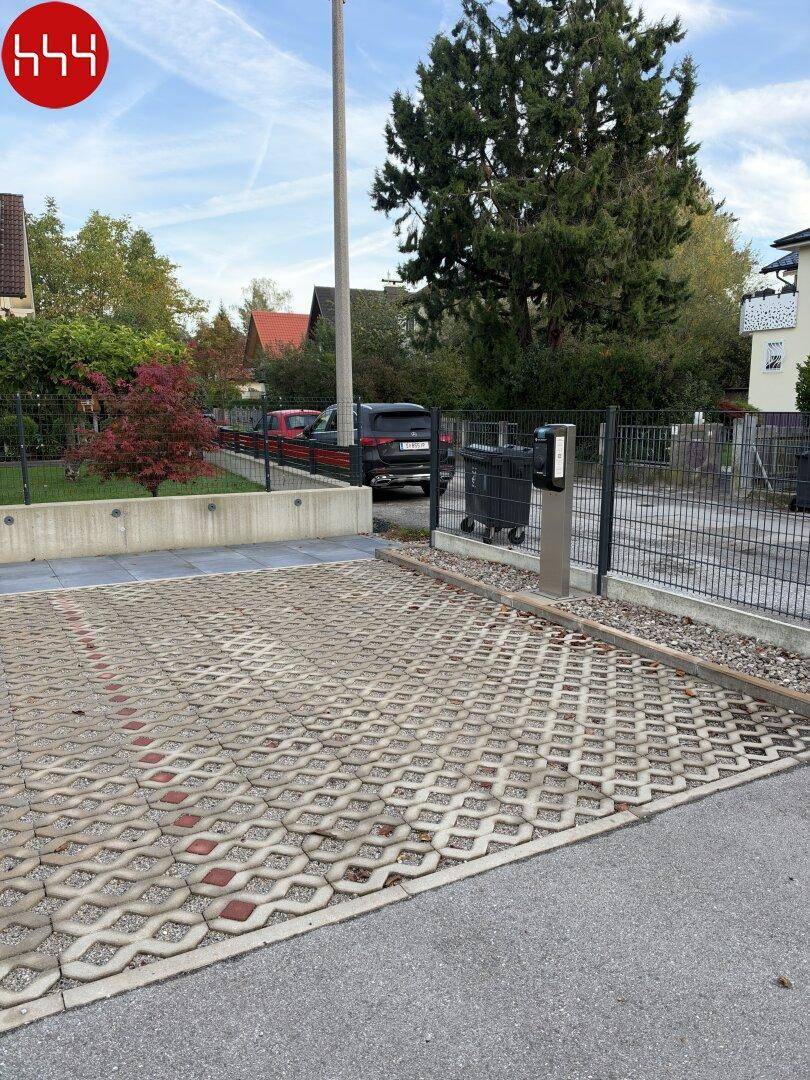 Außenparkplatz mit Rasengittersteinen, Ladestation für Elektrofahrzeuge und Mülltonnen im Freien.