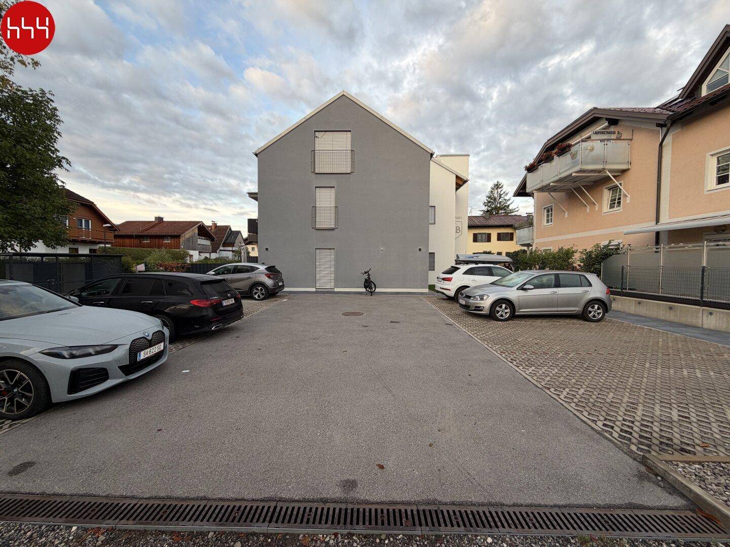 Moderne Gebäudefassade in Grau und Weiß mit vorgelagertem Parkplatz und geparkten Autos.