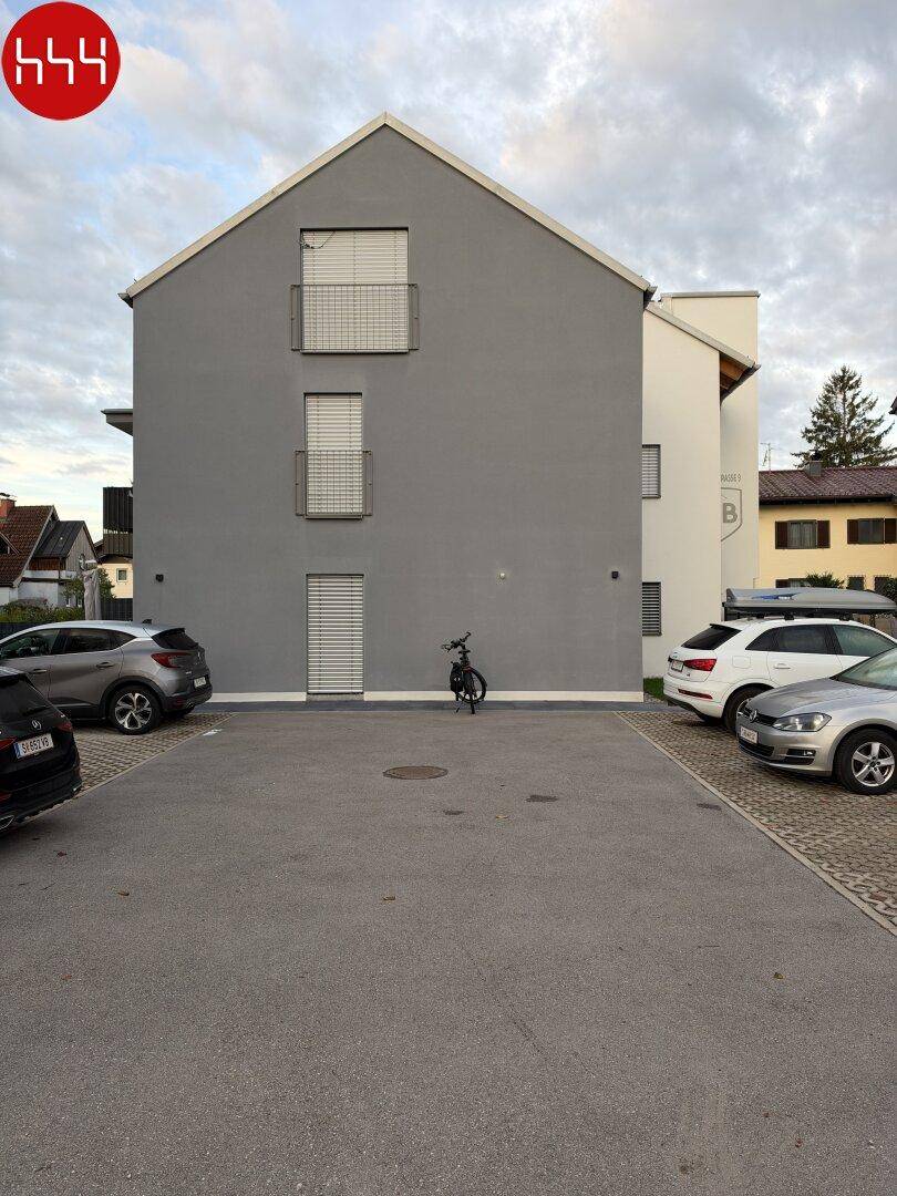Ansicht der modernen Gebäudefassade mit kleinen Balkonen und Rollläden, umgeben von einem Parkplatz.