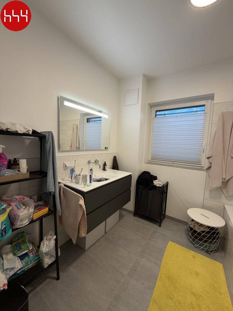 Helles Badezimmer mit modernem Waschtisch, beleuchtetem Spiegel und Fenster.