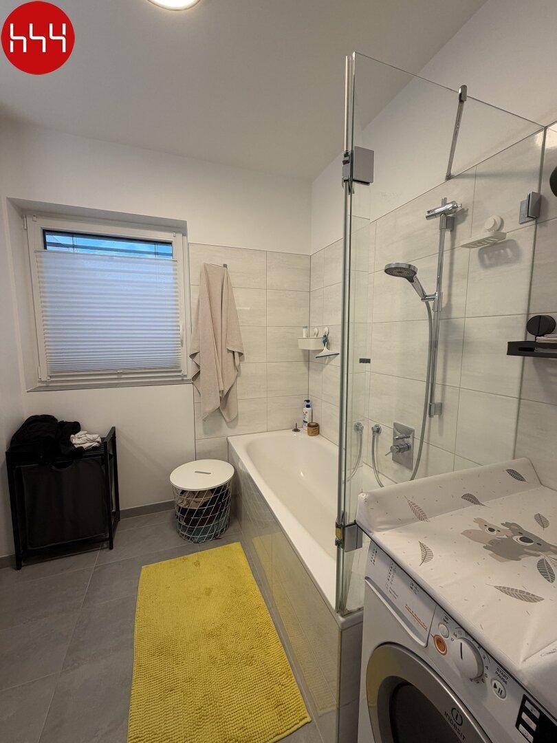 Funktionales Badezimmer mit Badewanne, integrierter Dusche und Waschmaschine.