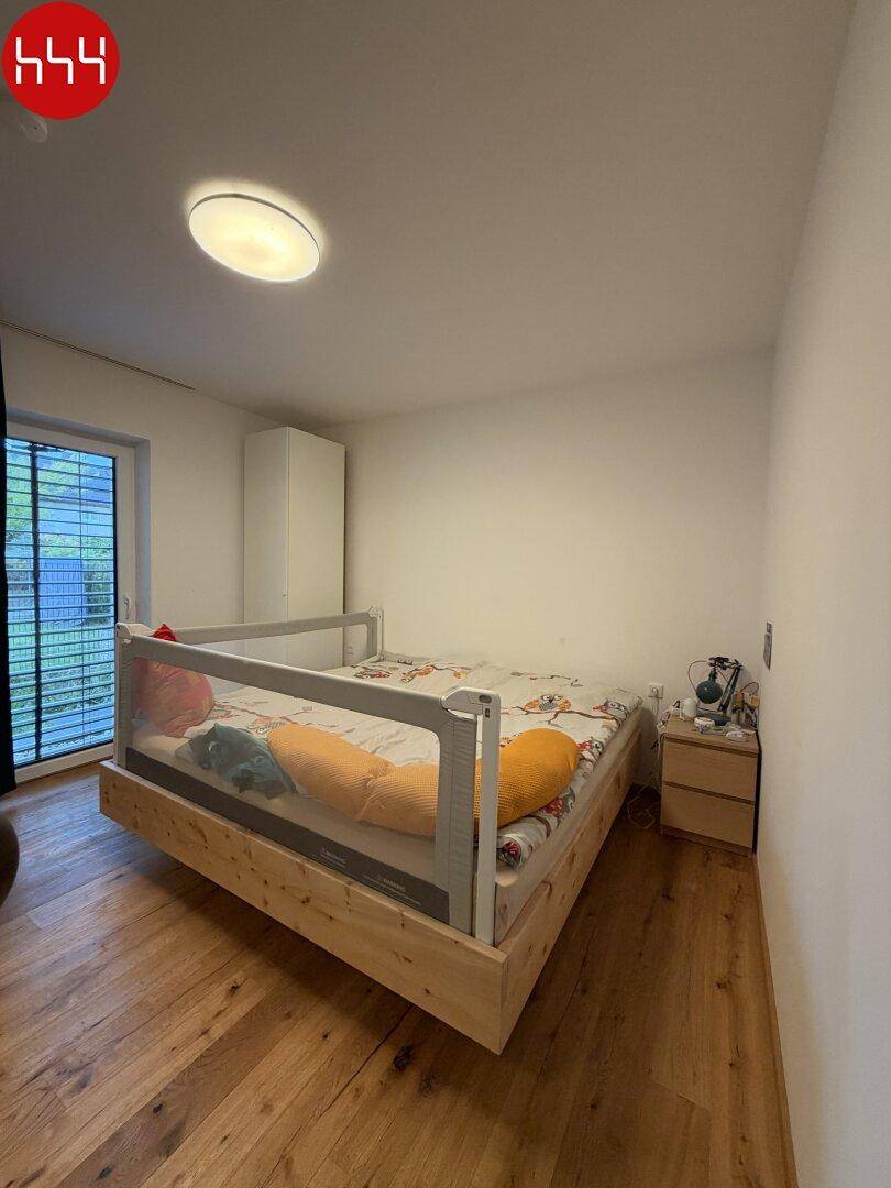 Schlafzimmer mit Holzboden, großem Fenster und einem modernen Bettgestell.