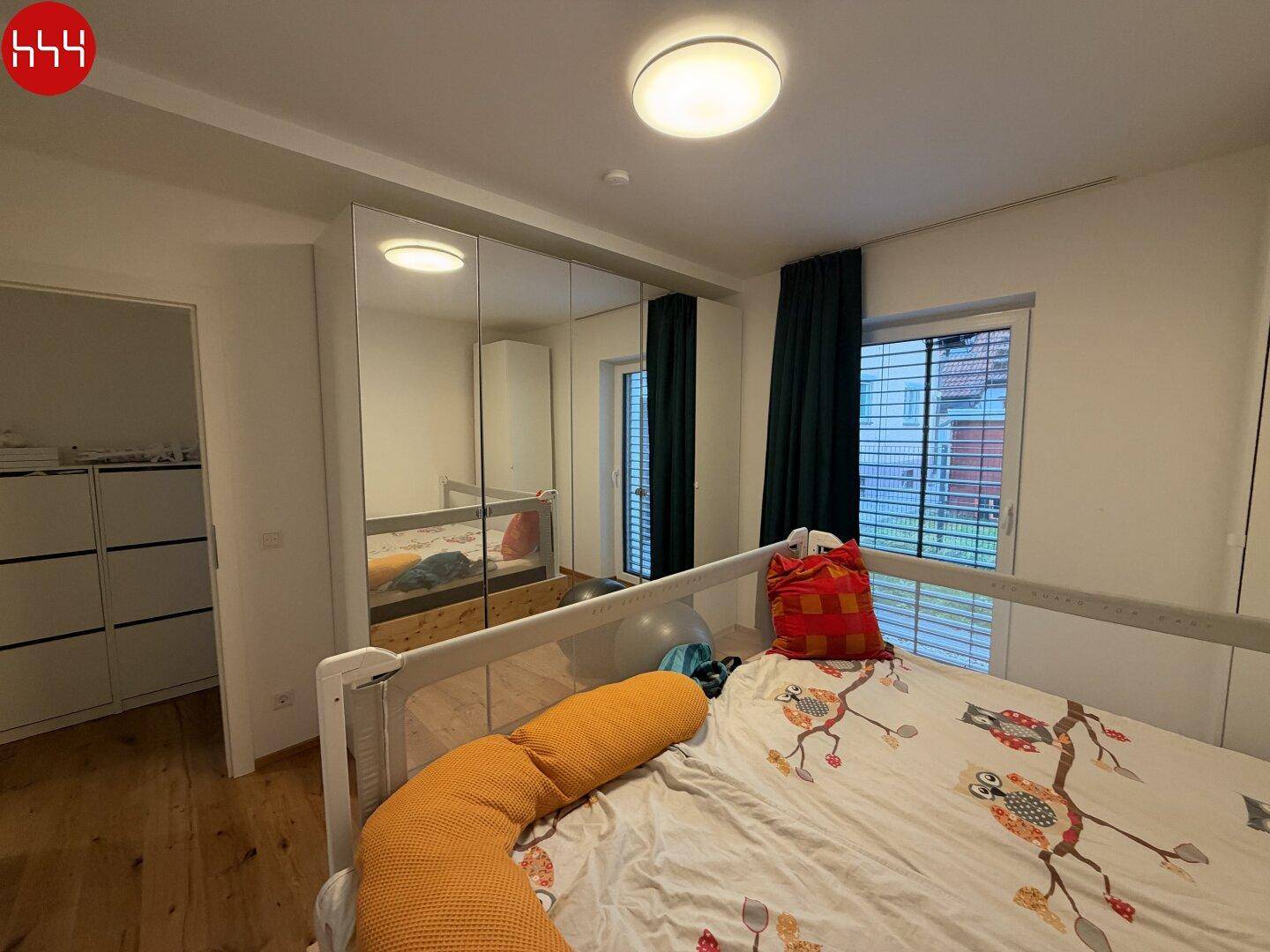 Schlafzimmer mit Spiegelschränken, Holzboden und Blick ins Grüne durch das Fenster.