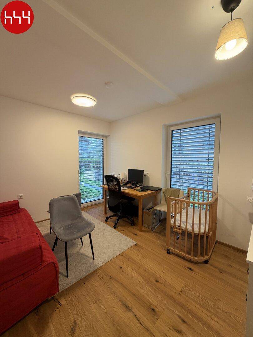 Helles Zimmer mit Holzboden, Schreibtisch und zwei großen Fenstern.