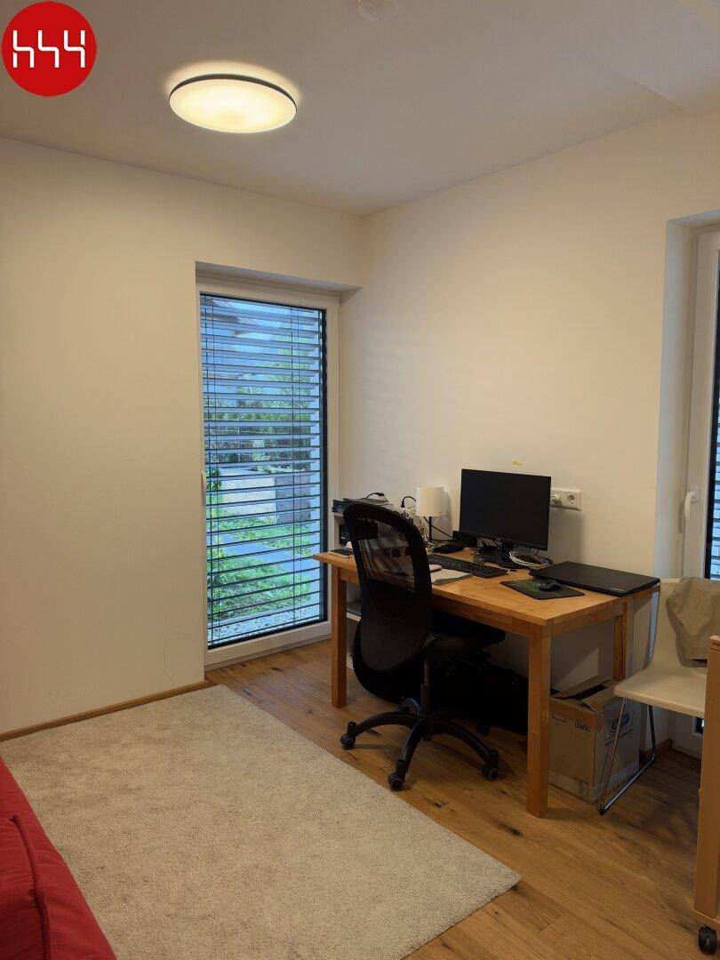 Ruhiges Arbeitszimmer mit Holzboden und Blick ins Grüne durch das Fenster.