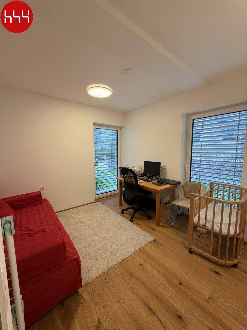 Geräumiges Zimmer mit rotem Sofa, Schreibtisch und Holzboden.