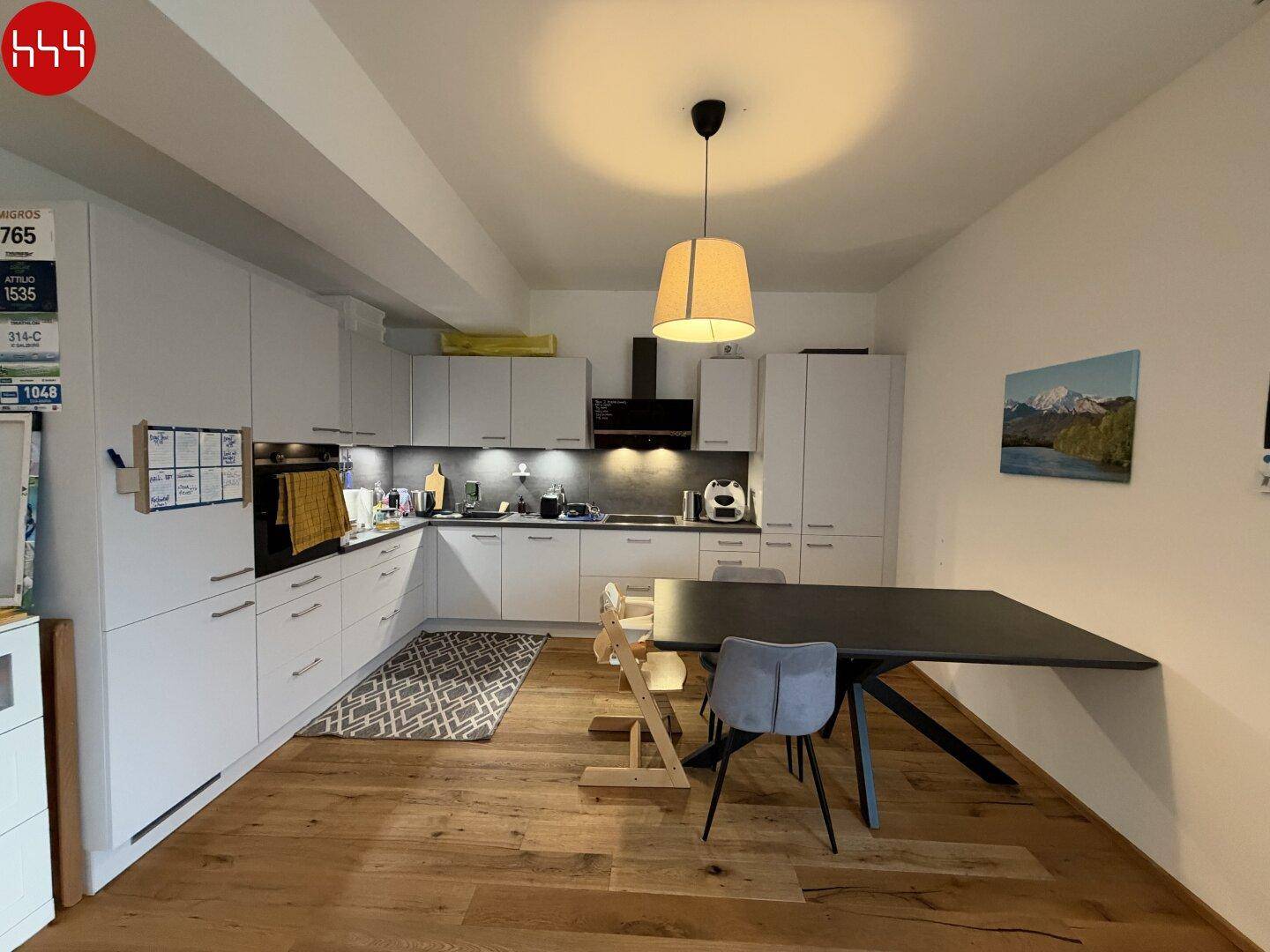 Moderne Küche mit weißen Schränken, Holzboden und integriertem Essbereich für die Familie.