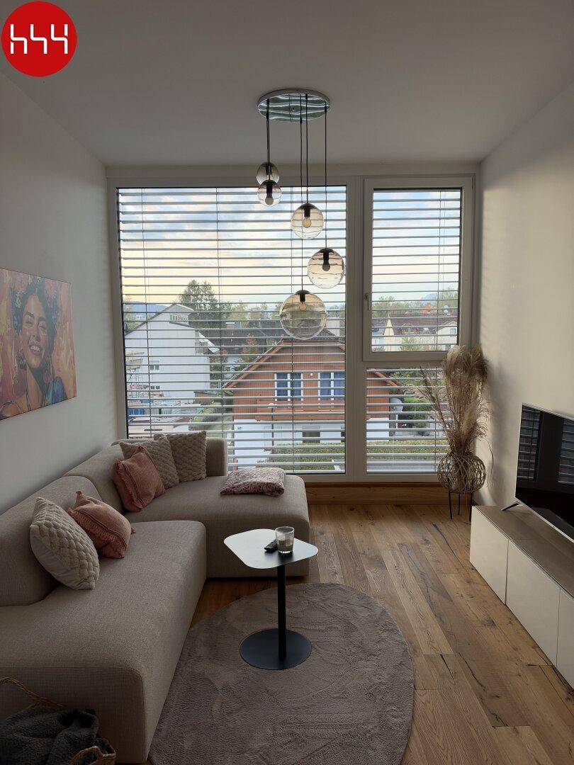 Heller Wohnbereich mit beigem Sofa, modernen Leuchten und Blick auf die Umgebung durch große Fenster.