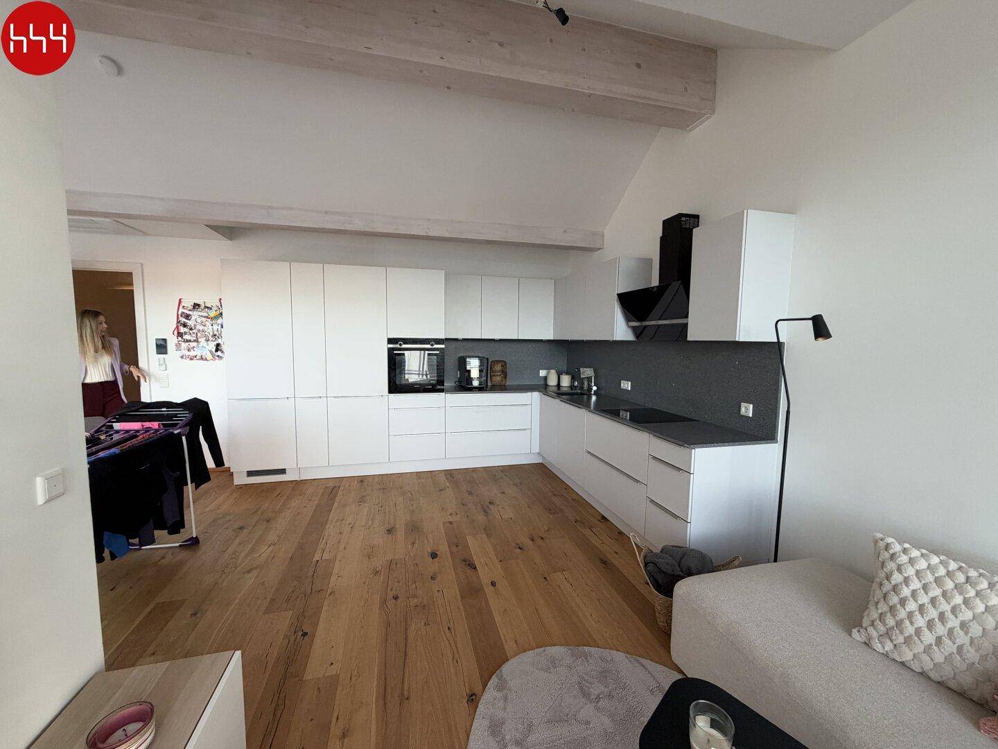 Offene Küche mit weißen Schränken und Holzboden, integriert in einen hellen Wohnbereich mit Dachschräge.
