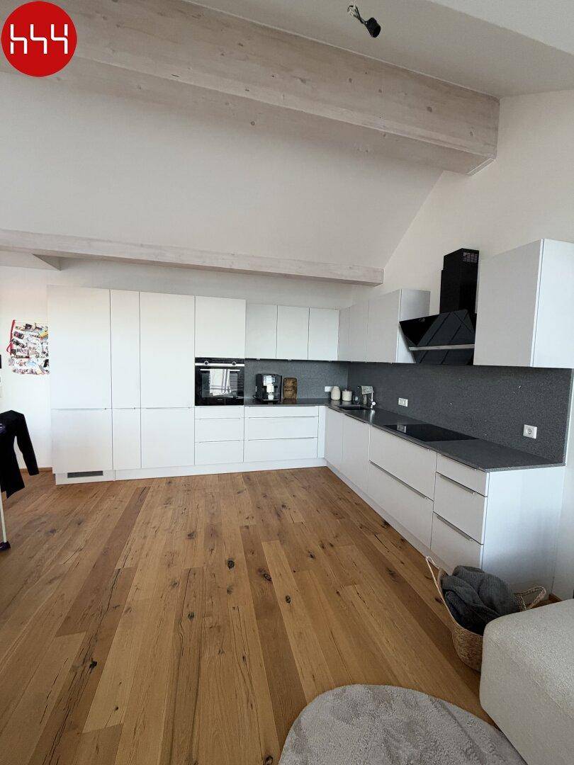 Stilvolle weiße Küche mit modernen Geräten und Holzbalken, die den offenen Wohnraum prägen.