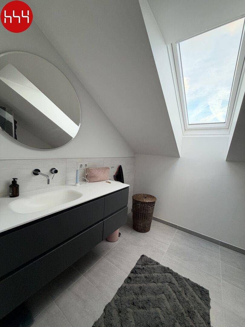 Helles Badezimmer mit Dachfenster, modernem Waschtisch und großem runden Spiegel.
