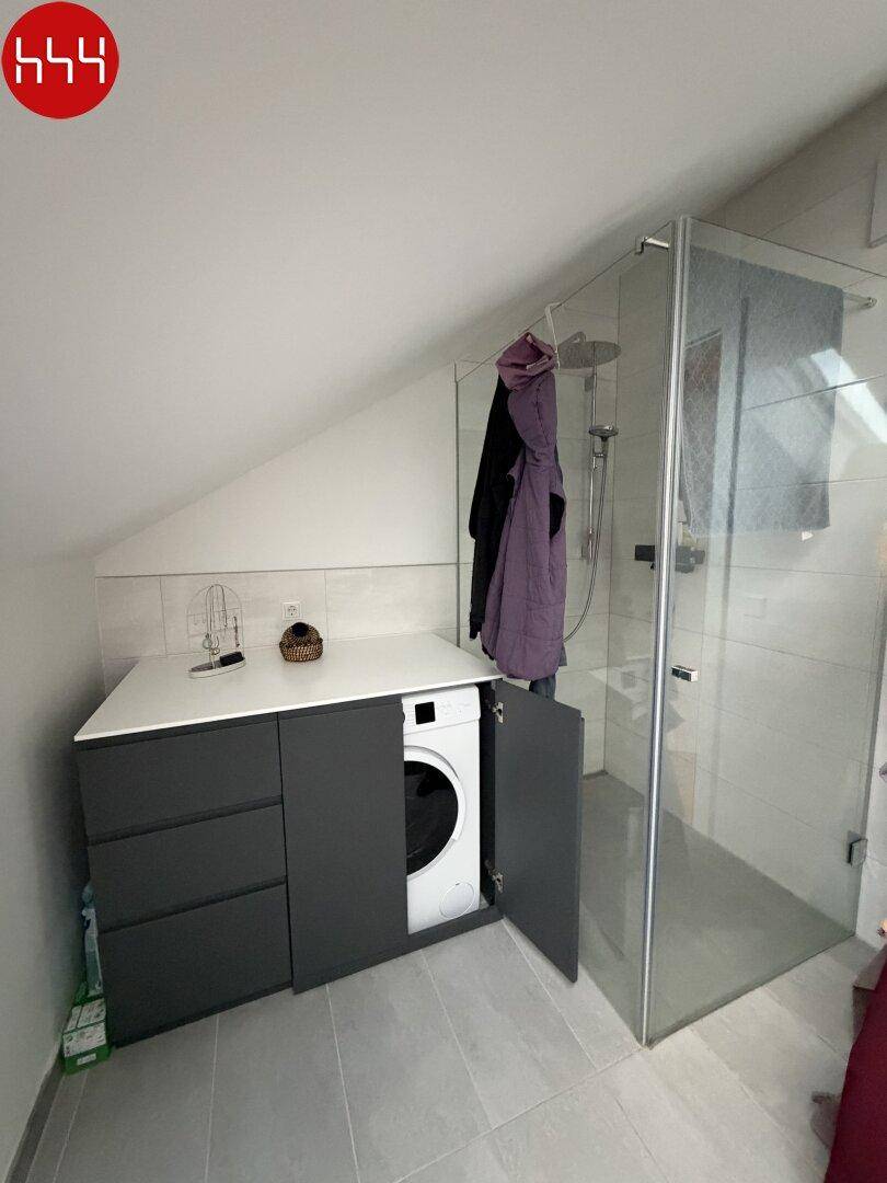 Funktionales Badezimmer mit integrierter Waschmaschine, begehbarer Dusche und modernem Waschtisch.