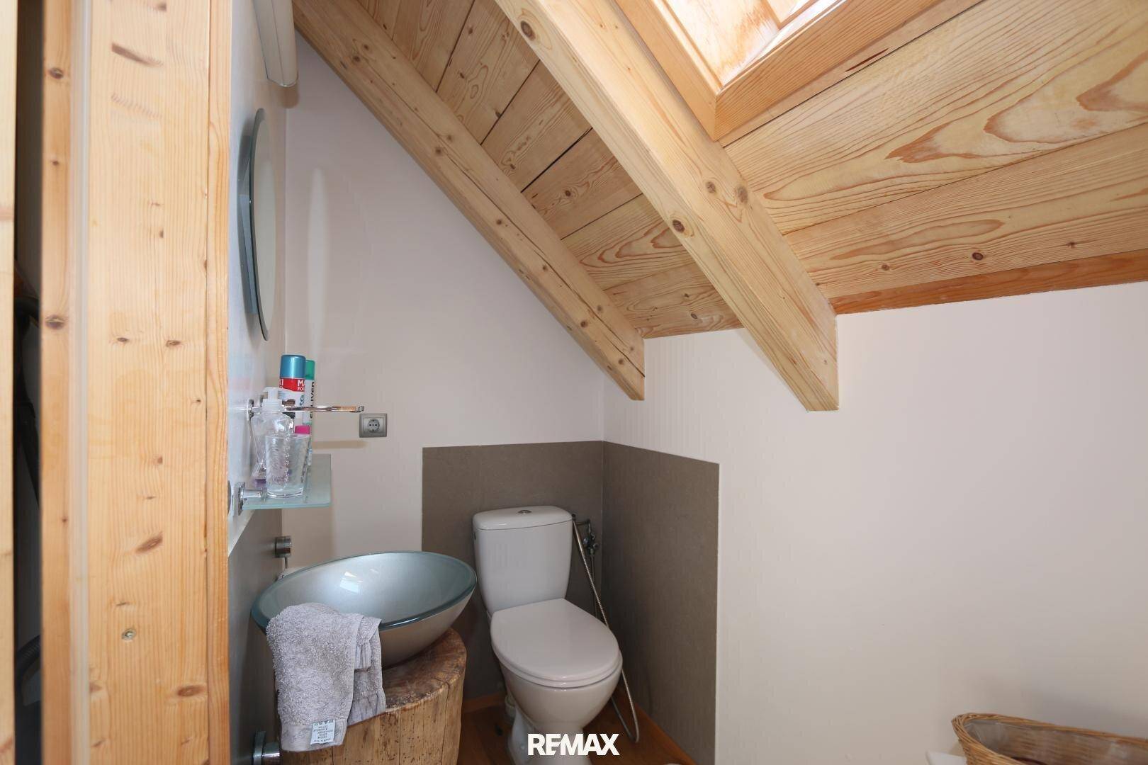Kleines Gäste-WC im Dachgeschoss mit Dachfenster, Holzbalken und einem einzigartigen Waschbecken auf einem Holzstamm.