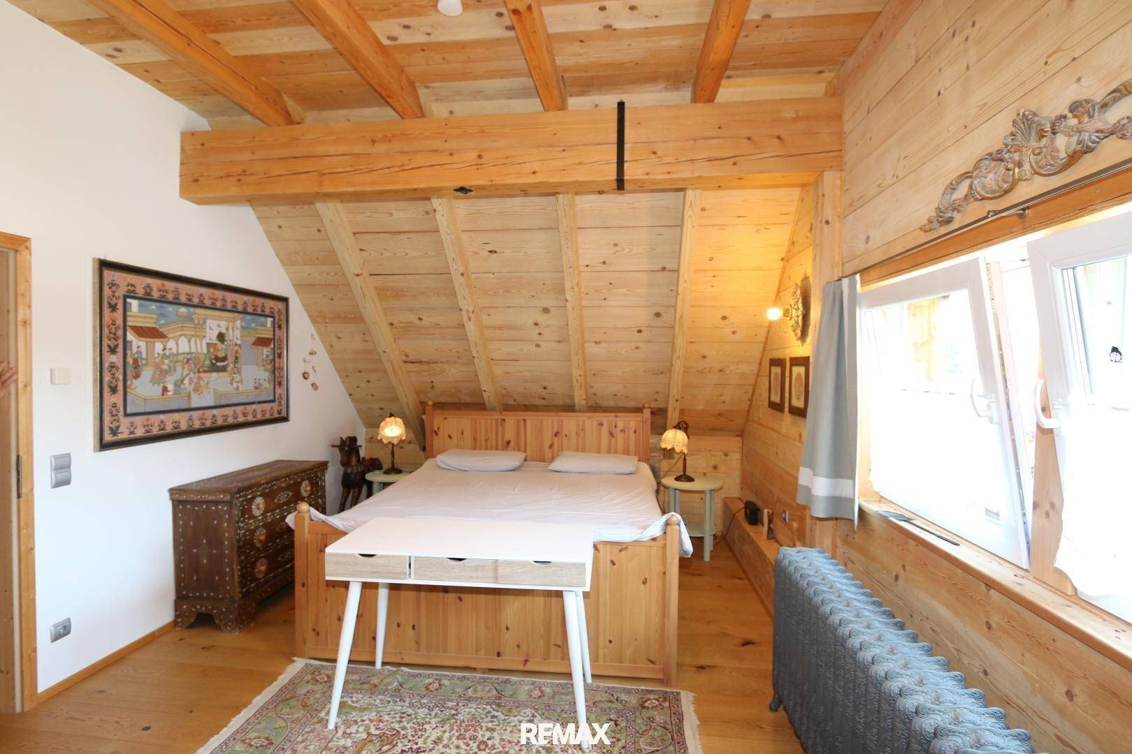 Gemütliches Schlafzimmer im Dachgeschoss mit Holzbalken, schrägen Wänden und einem traditionellen Holzdoppelbett.