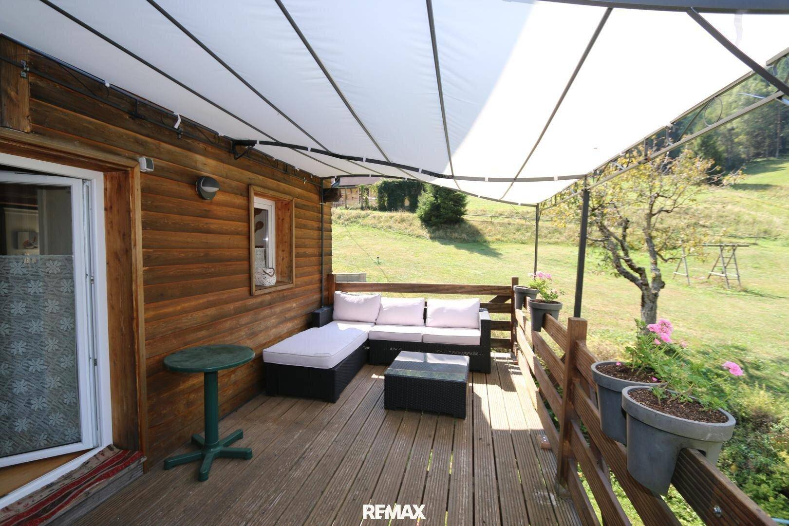 Überdachter Balkon mit Loungemöbeln und Blick auf die grüne Landschaft.