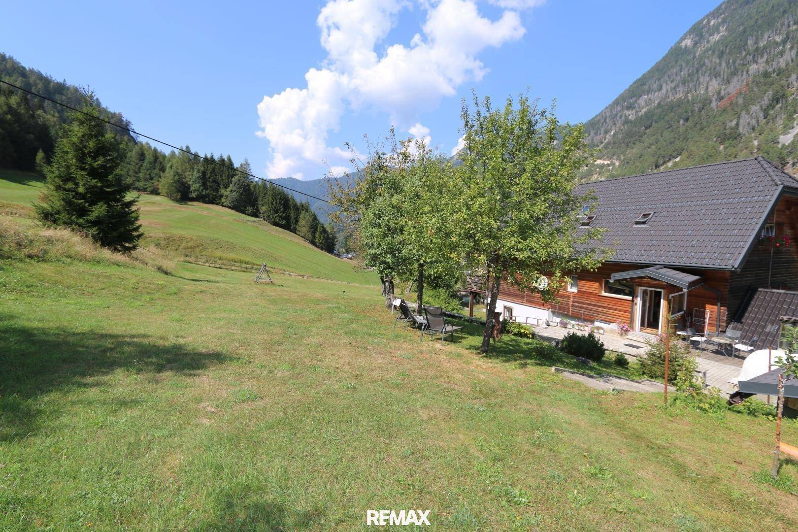Weitläufige grüne Wiesenfläche neben dem Holzhaus mit Blick auf die Berge.