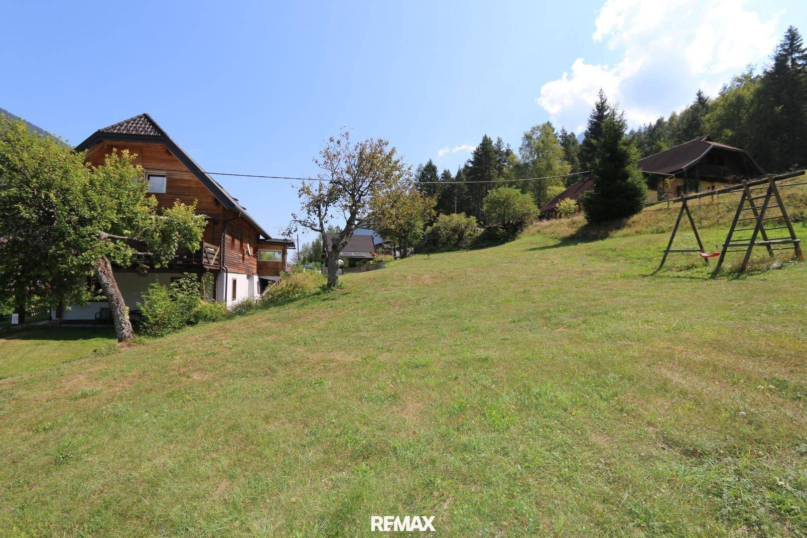 Große, sonnige Wiesenfläche mit Schaukelgestell und Blick auf die bewaldeten Hügel.