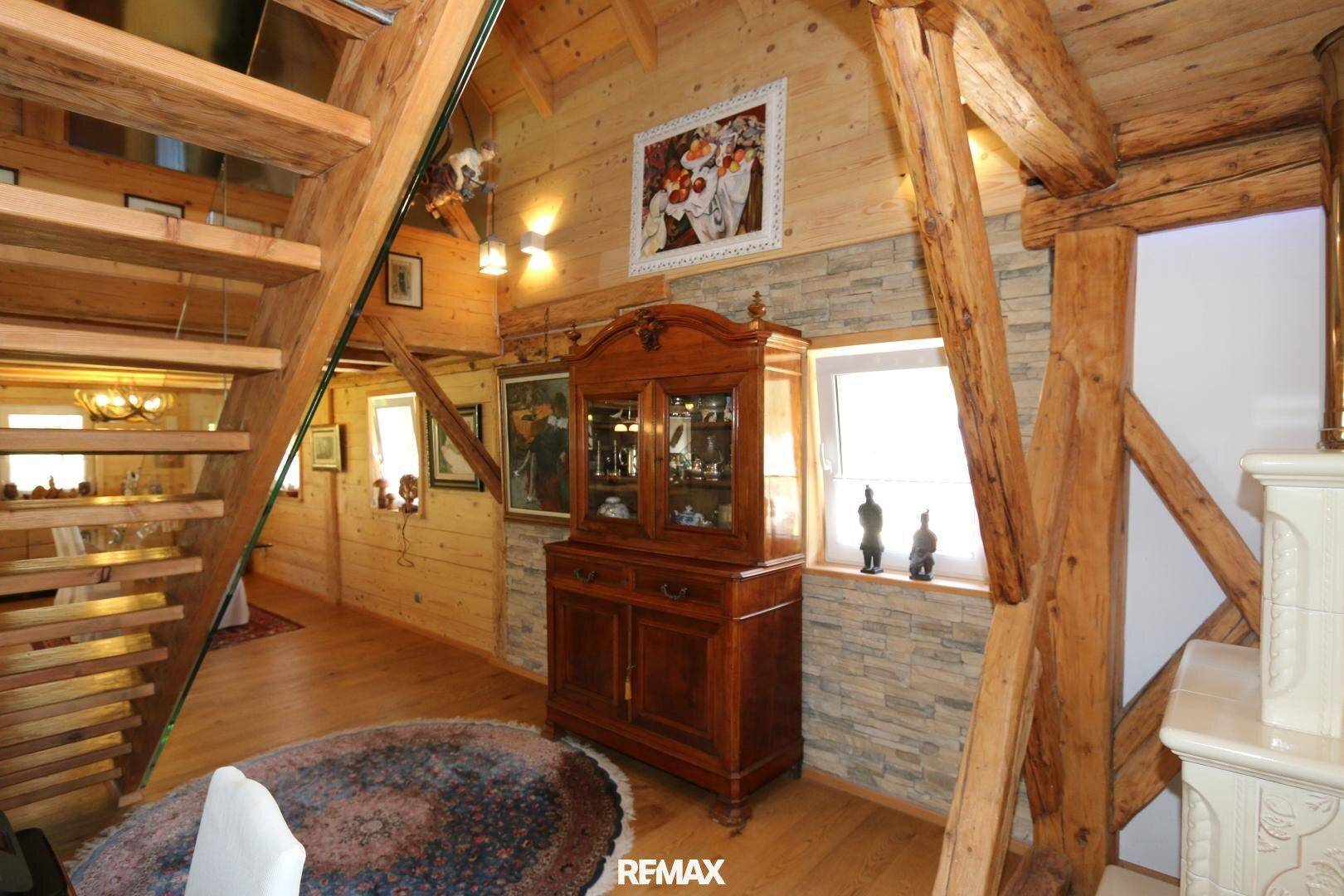 Heller Flur mit Holztreppe, Holzbalken und dekorativer Steinwand, sehr einladend.