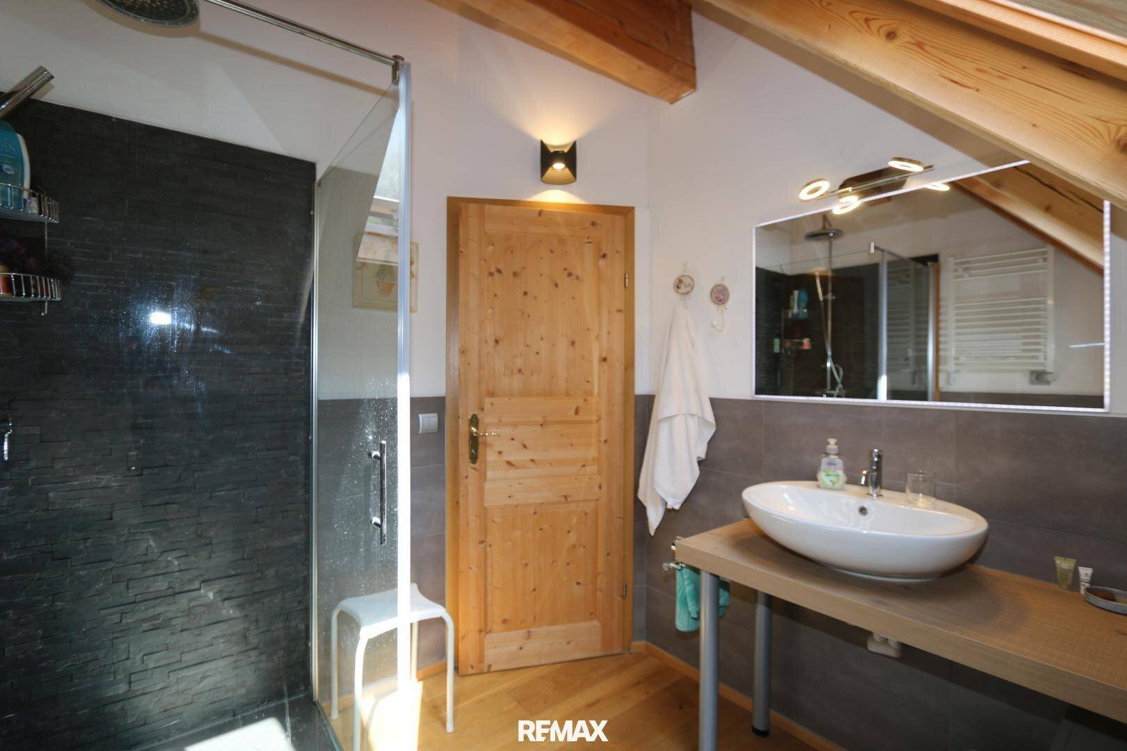 Modernes Badezimmer mit begehbarer Dusche, Holztür und Dachschräge, sehr hell.