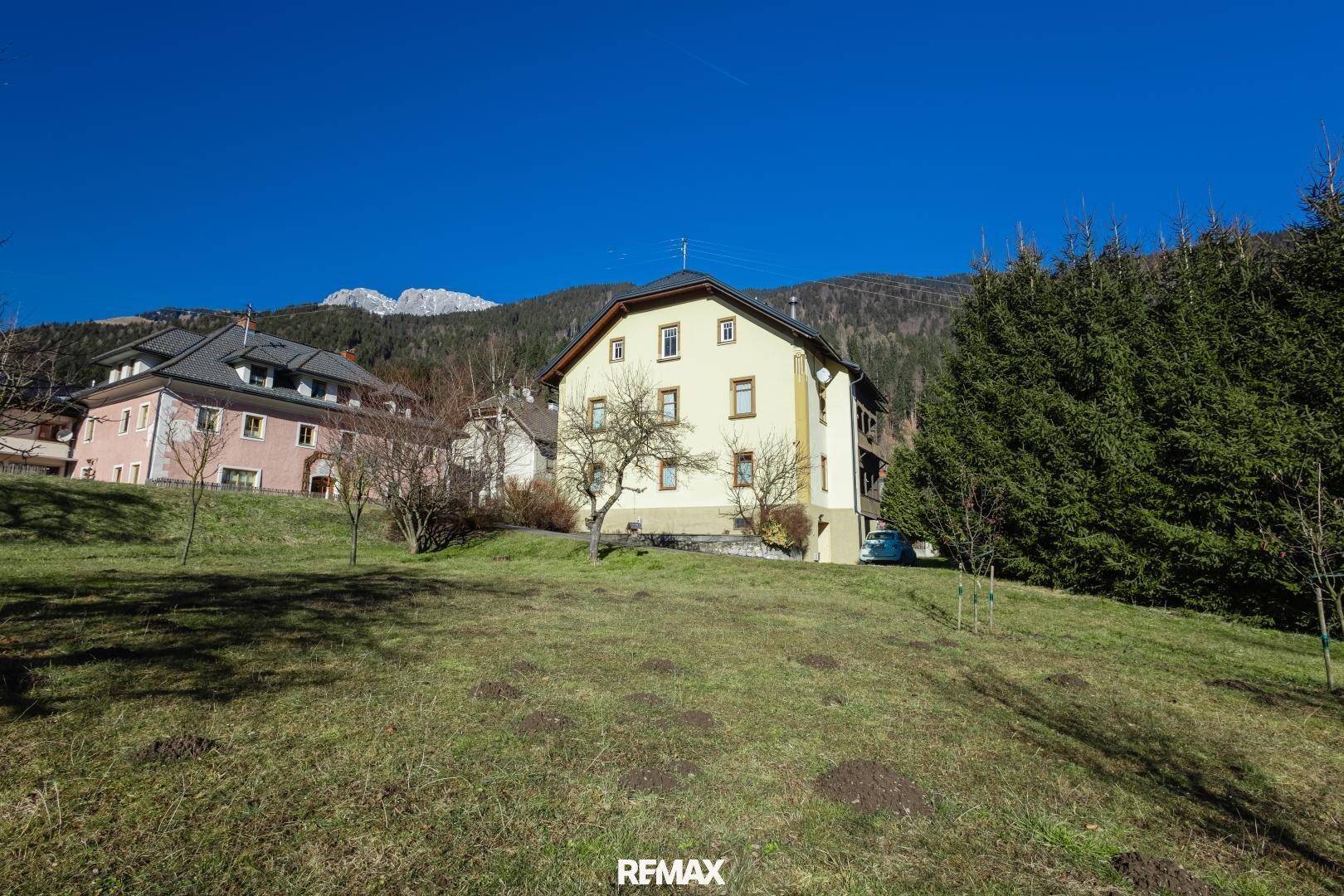 Haus auf einem grünen Hügel mit weitem Blick auf die umliegende Berglandschaft.