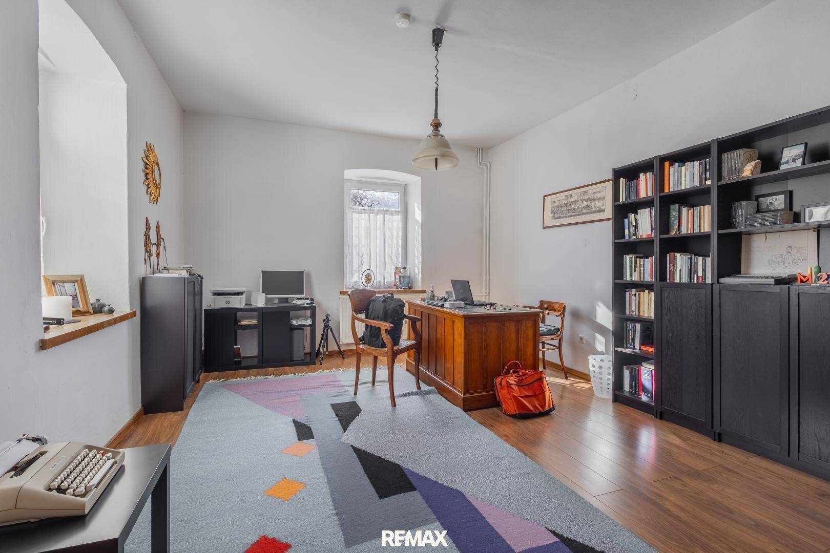 Helles Arbeitszimmer mit großem Holzschreibtisch, Bücherregalen und farbenfrohem Teppich.
