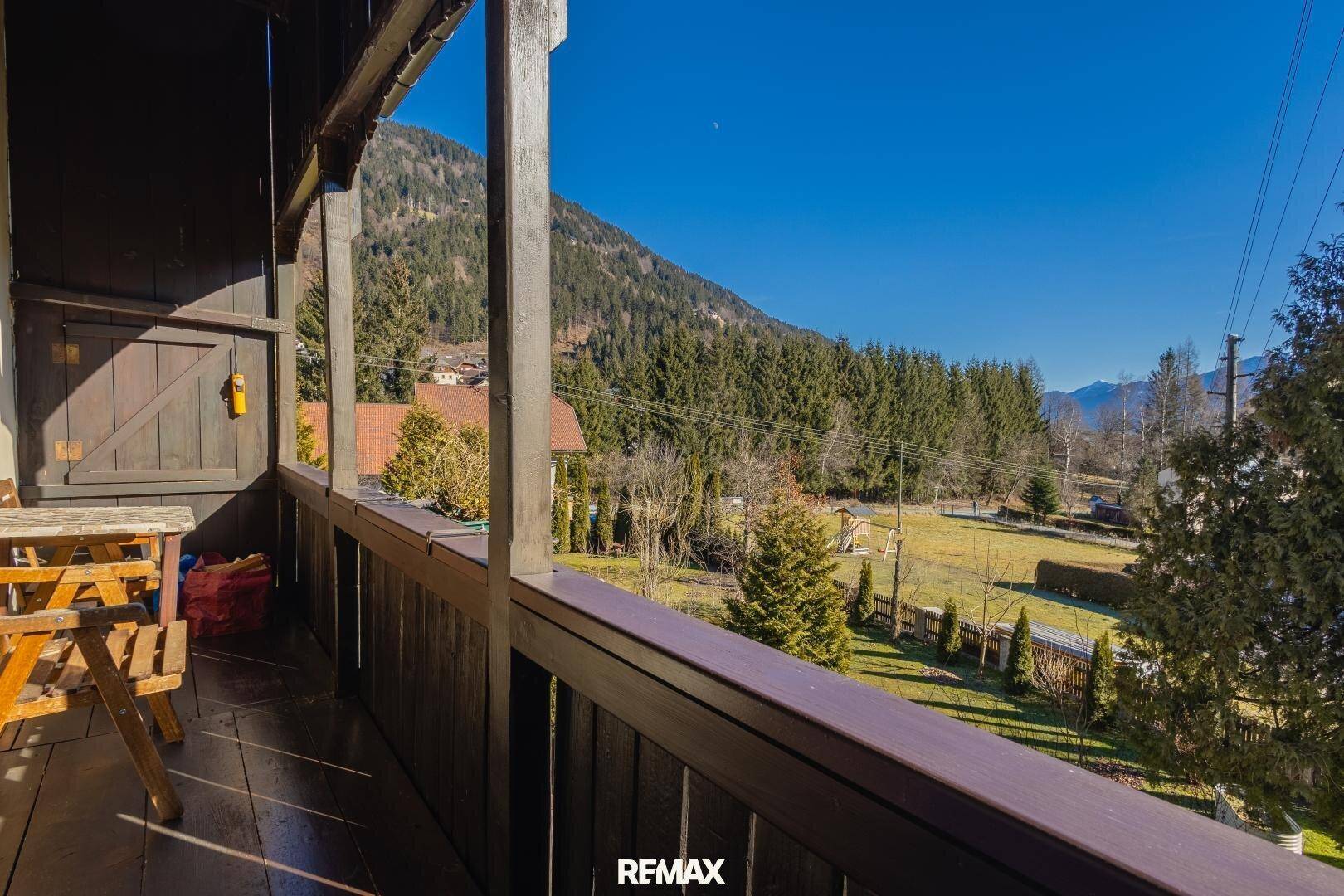 Rustikaler Holzbalkon mit Bergblick und Sitzgelegenheit, ideal für sonnige Stunden im Freien.