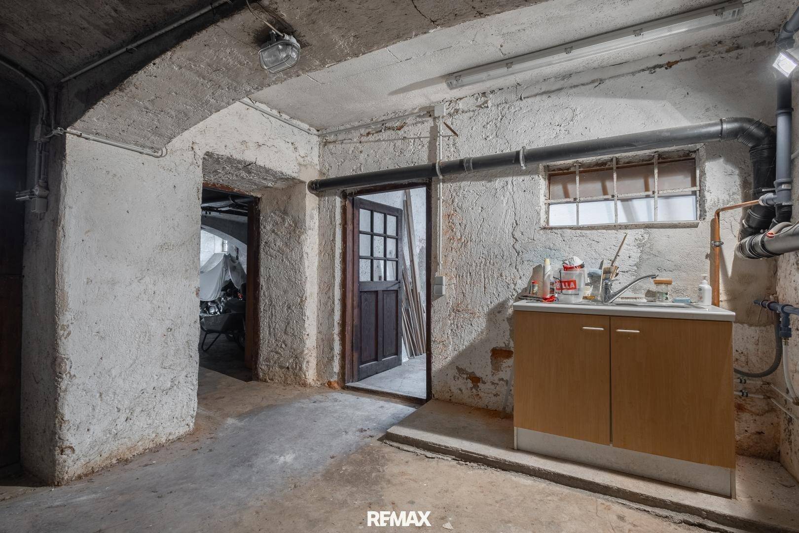 Kellerraum mit Waschbecken und sichtbaren Installationen, ideal als Hauswirtschaftsraum.