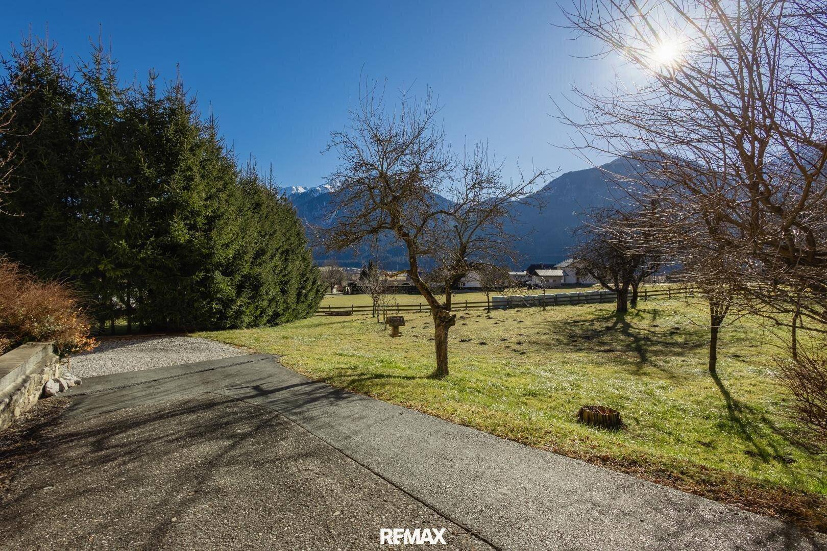 Zufahrt durch eine grüne Landschaft mit Bäumen und Panoramablick auf die Berge.